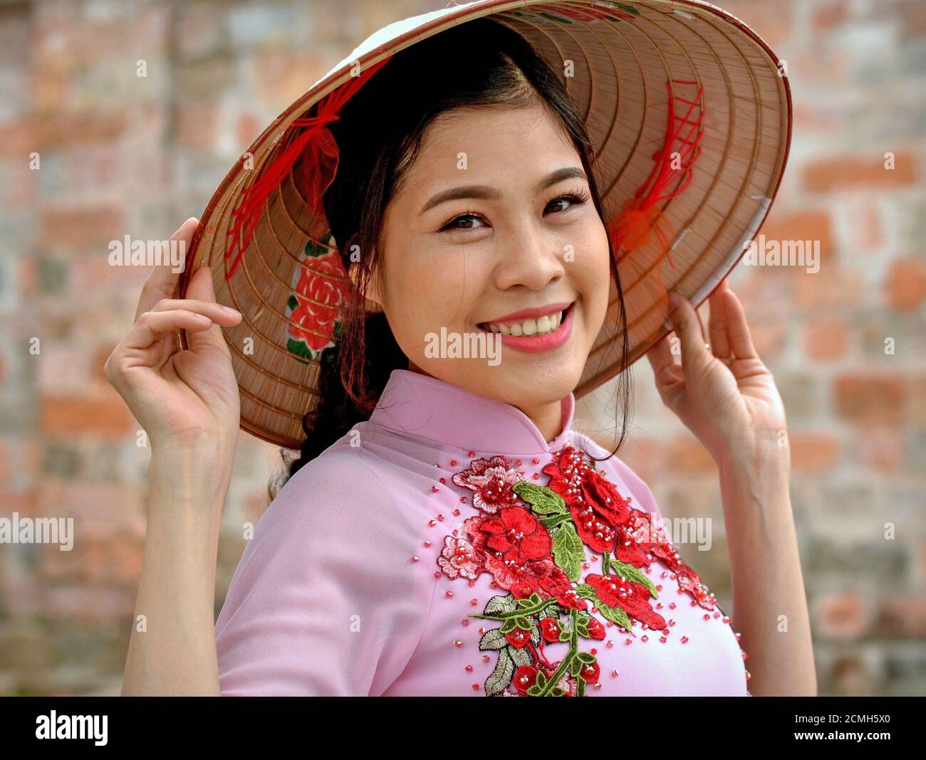 Belle jeune femme vietnamienne tient le bord de son chapeau conique  asiatique avec les deux mains et sourires à la caméra Photo Stock - Alamy