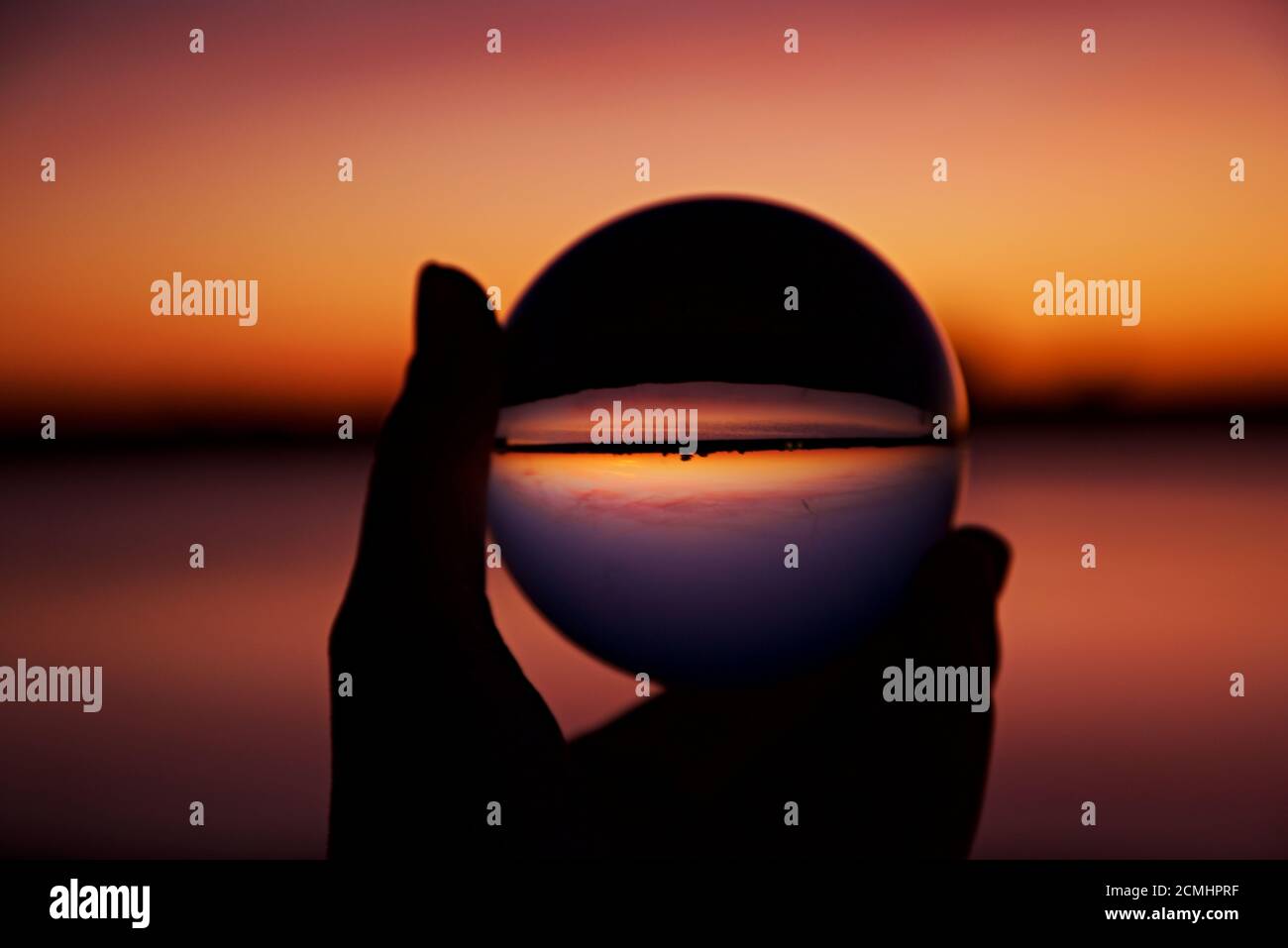 Coucher de soleil sur l'île d'Assateague au-dessus des marais, baie d'eau salée reflétée dans la boule de cristal tenue par une main. Banque D'Images