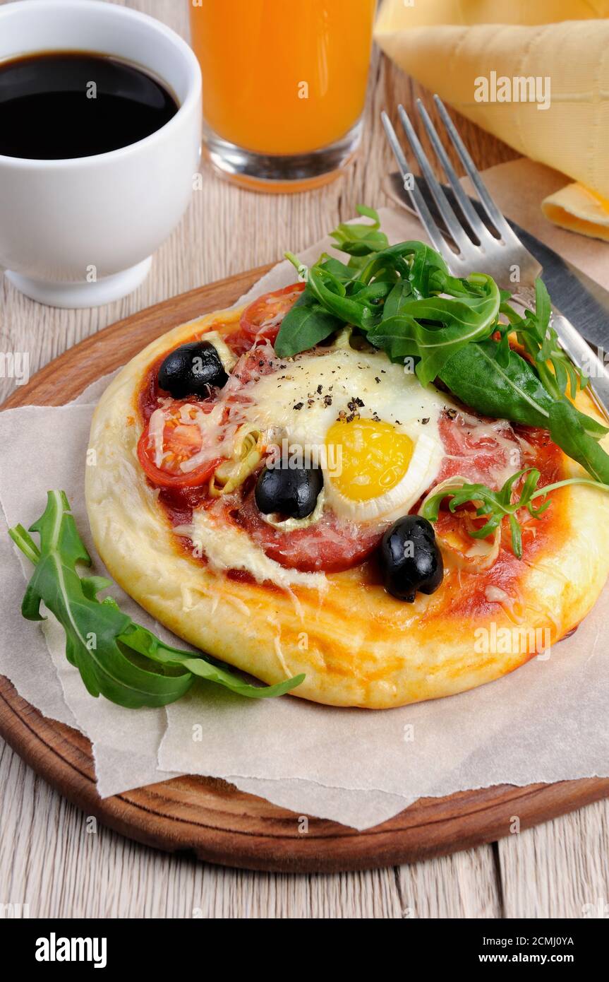 Mini pizza avec de la saucisse et l'oeuf et la roquette, une tasse de café pour le petit déjeuner Banque D'Images