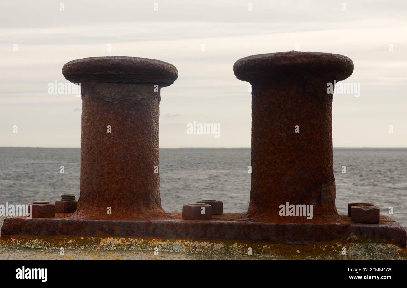 Bollards rouillés pour fixer les cordes de navires sur un mur du port avec vue sur la mer Banque D'Images