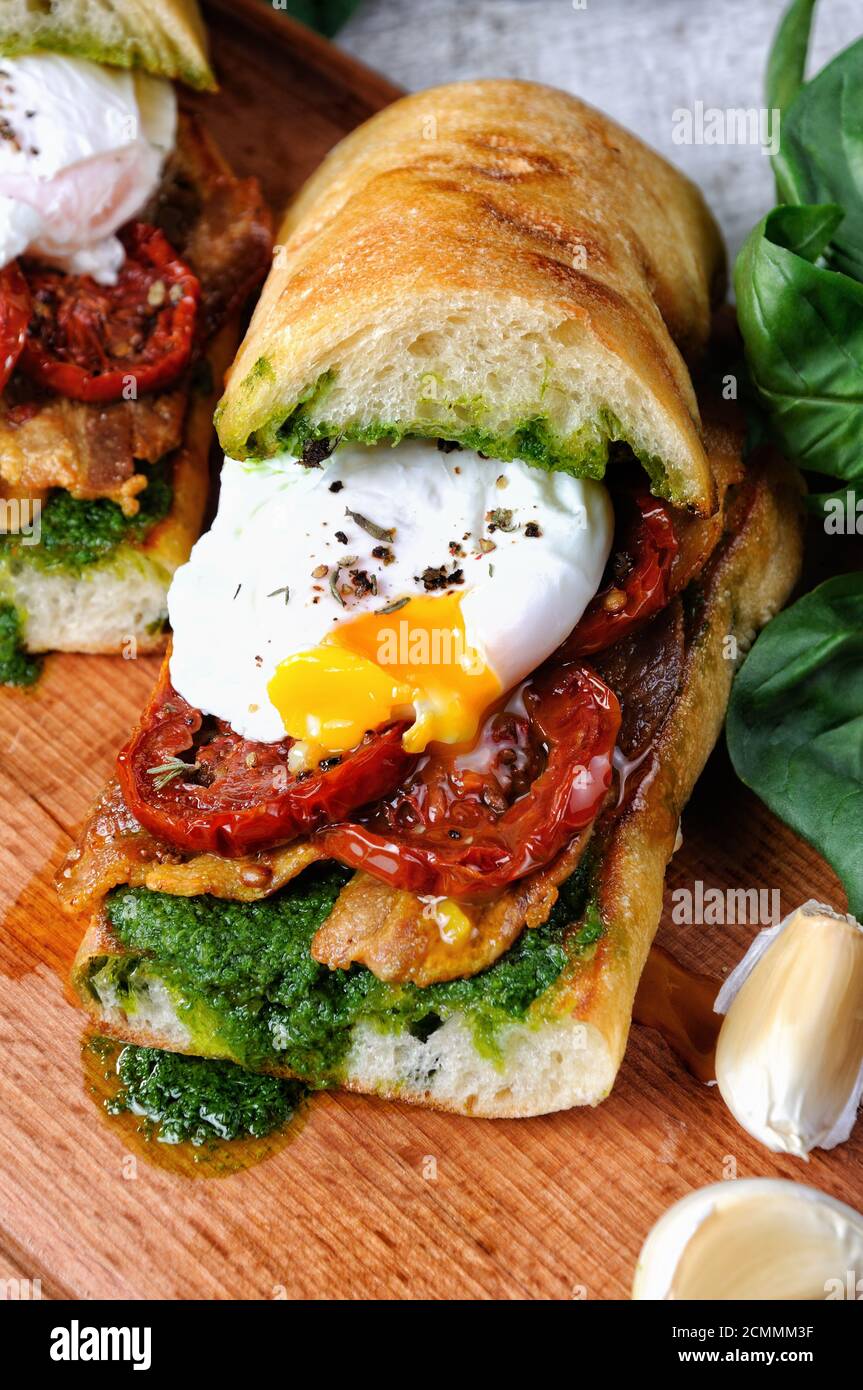 Ciabatta grillé au pesto, tranches de bacon, tomates séchées au soleil et œuf poché Banque D'Images