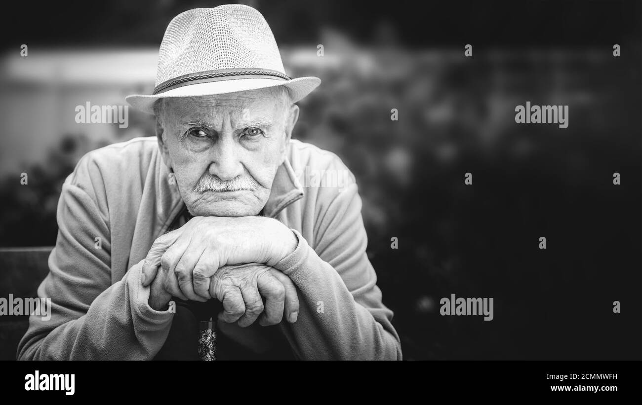 triste, sérieux, vieux homme dans un chapeau est assis dans un jardin en plein air. le concept de solitude et de vieillesse solitaire. Portrait en noir et blanc Banque D'Images