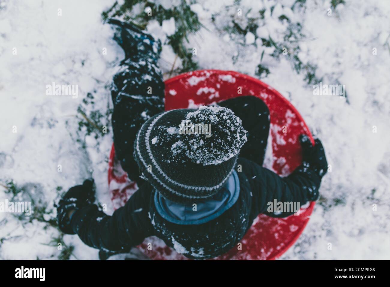 Cristaux de glace intégrés dans le chapeau de bas de Noël bonnet beanie de jeune garçon tandis qu'il glisse sur la soucoupe ronde traîneau pendant la tempête de neige hiver froide. Banque D'Images