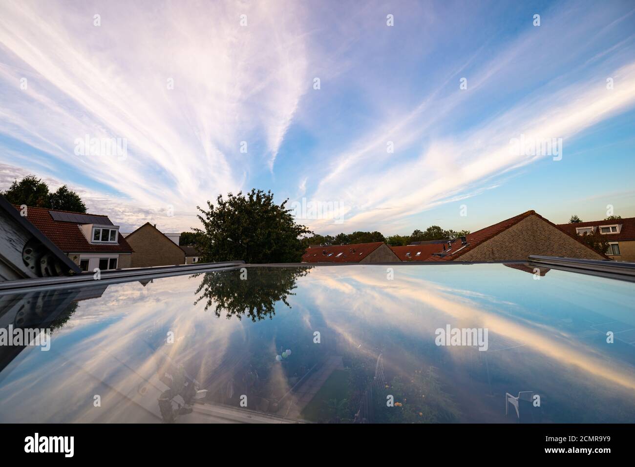 Les nuages de Cirrus qui semblent venir d'un point sont reflétés dans la vitre d'une fenêtre de toit. En météorologie, ces nuages sont connus sous le nom de Cirrus radiatus. Banque D'Images