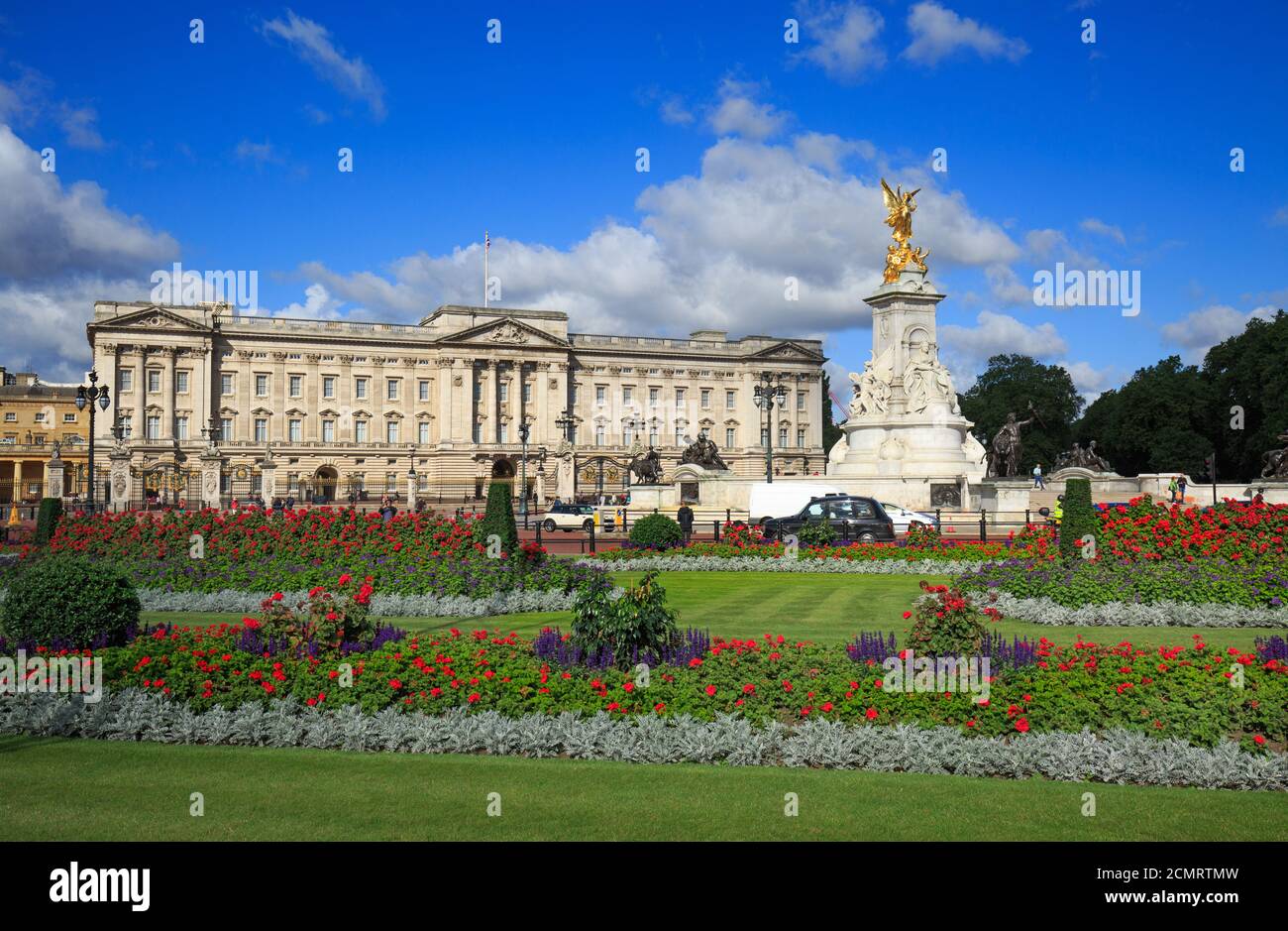 Vue panoramique de Buckingham Palace prise de Green Park, avec des massifs fleuris en pleine floraison contre un ciel bleu nuageux et pittoresque et le monument de la Reine Victoria. Banque D'Images