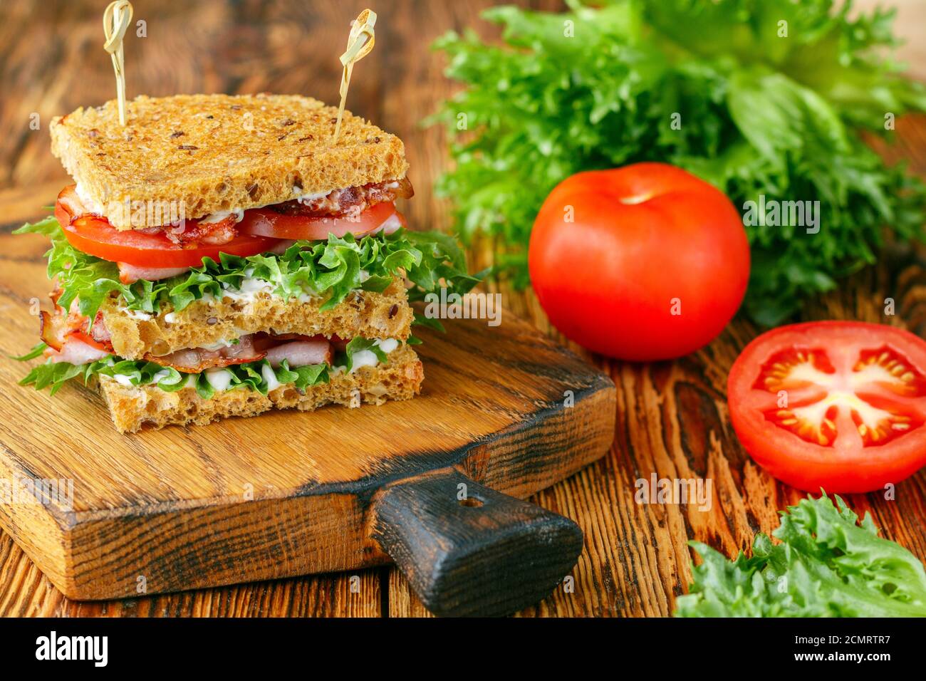 Délicieux sandwichs club avec salade verte laitue, jambon, bacon, tomates fraîches et sauce sur une planche à découper en bois. Concept déjeuner. Mise au point sélective Banque D'Images