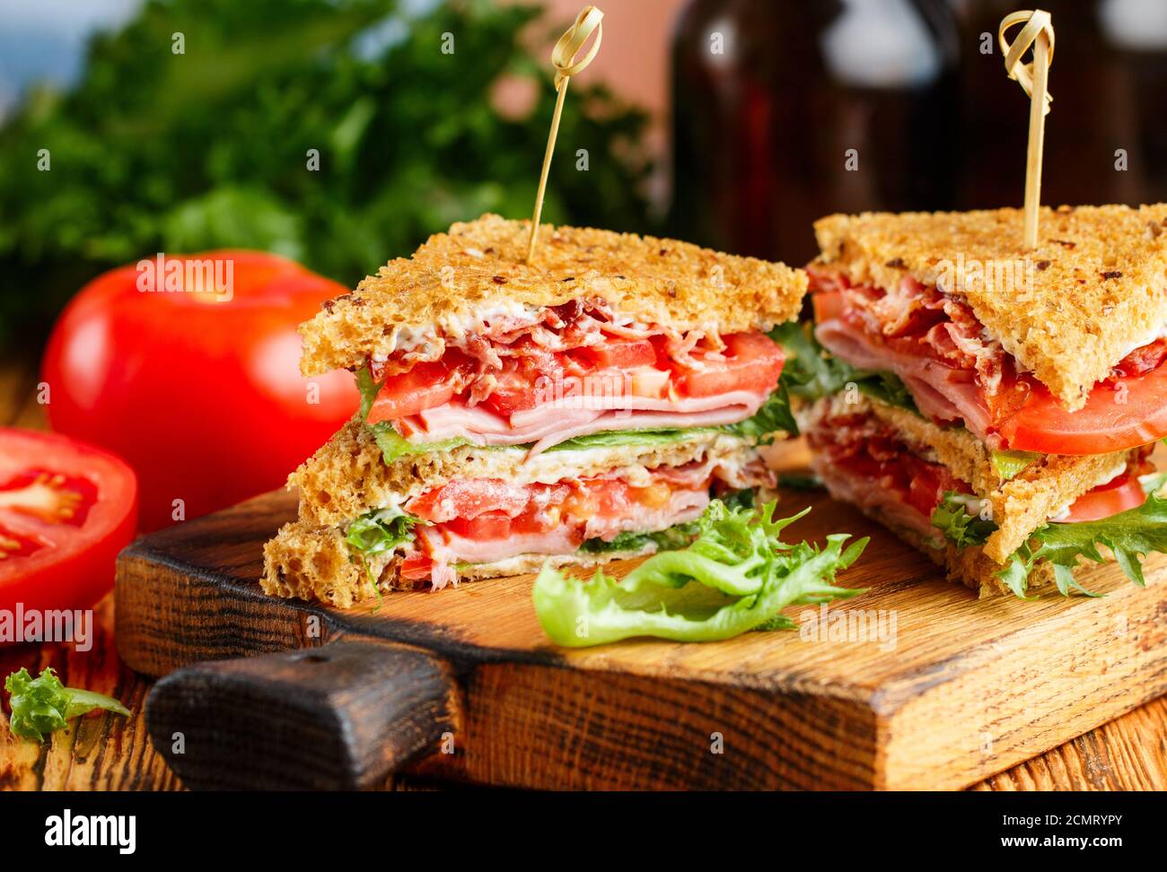 Délicieux sandwichs club avec salade verte laitue, jambon, bacon, tomates fraîches et sauce sur une planche à découper en bois. Concept déjeuner. Mise au point sélective Banque D'Images