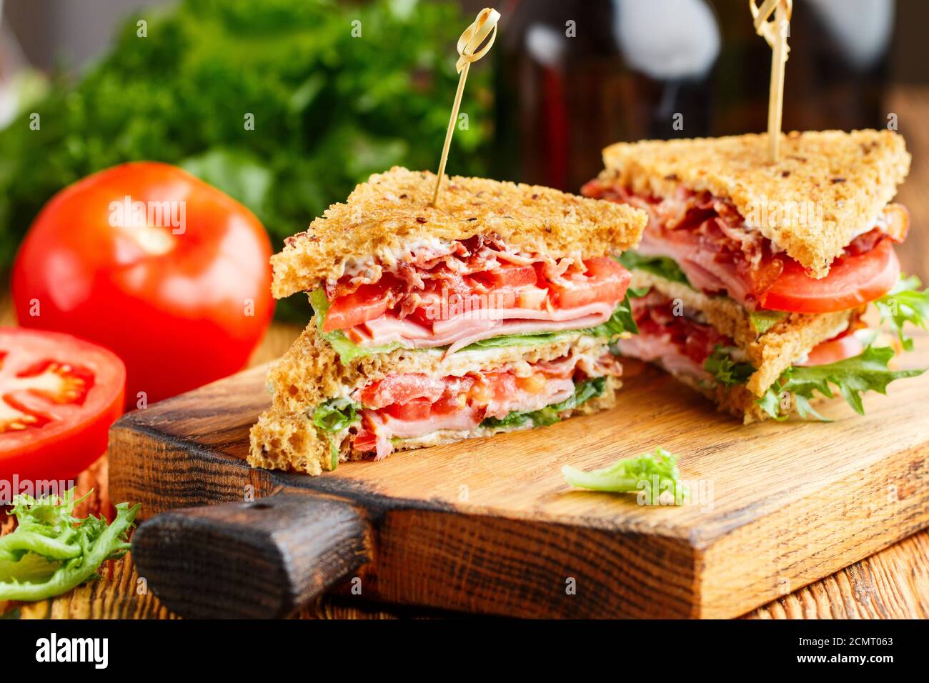 Délicieux sandwichs club avec salade verte laitue, jambon, bacon, tomates fraîches et sauce sur une planche à découper en bois. Concept déjeuner. Mise au point sélective Banque D'Images