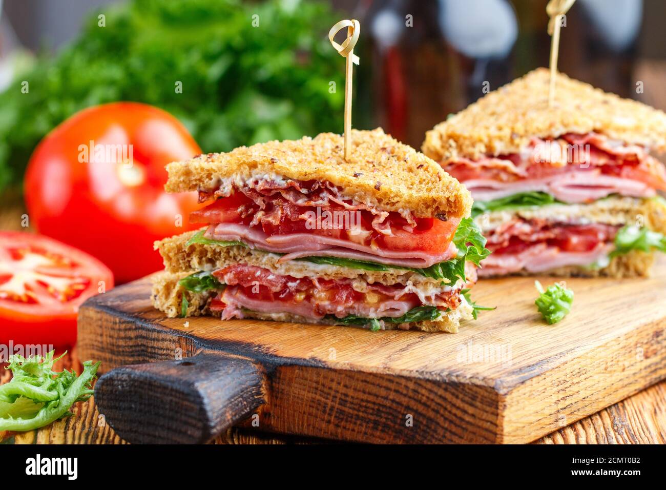 Délicieux sandwichs club avec salade verte laitue, jambon, bacon, tomates fraîches et sauce sur une planche à découper en bois. Concept déjeuner. Mise au point sélective Banque D'Images