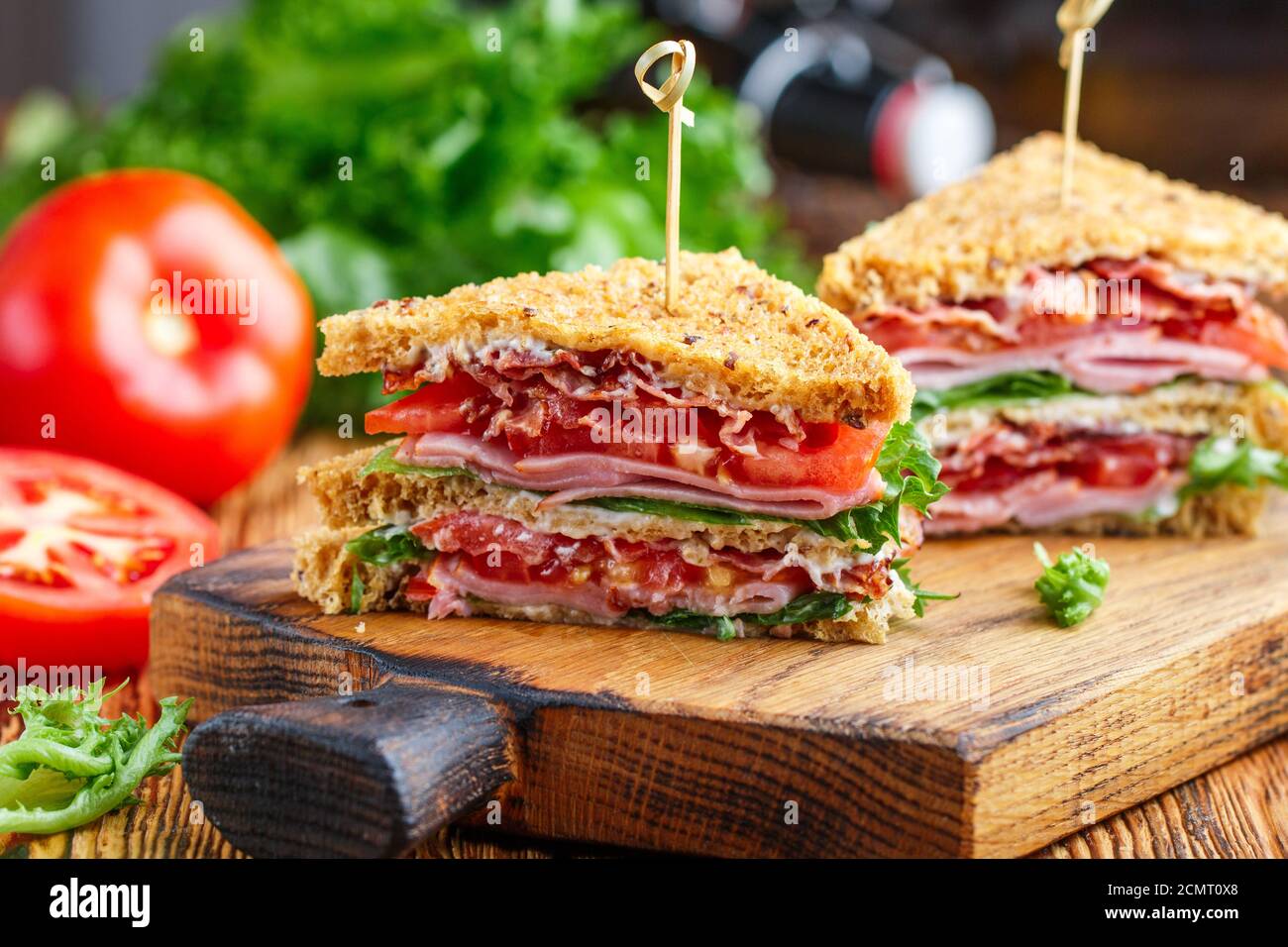 Délicieux sandwichs club avec salade verte laitue, jambon, bacon, tomates fraîches et sauce sur une planche à découper en bois. Concept déjeuner. Mise au point sélective Banque D'Images