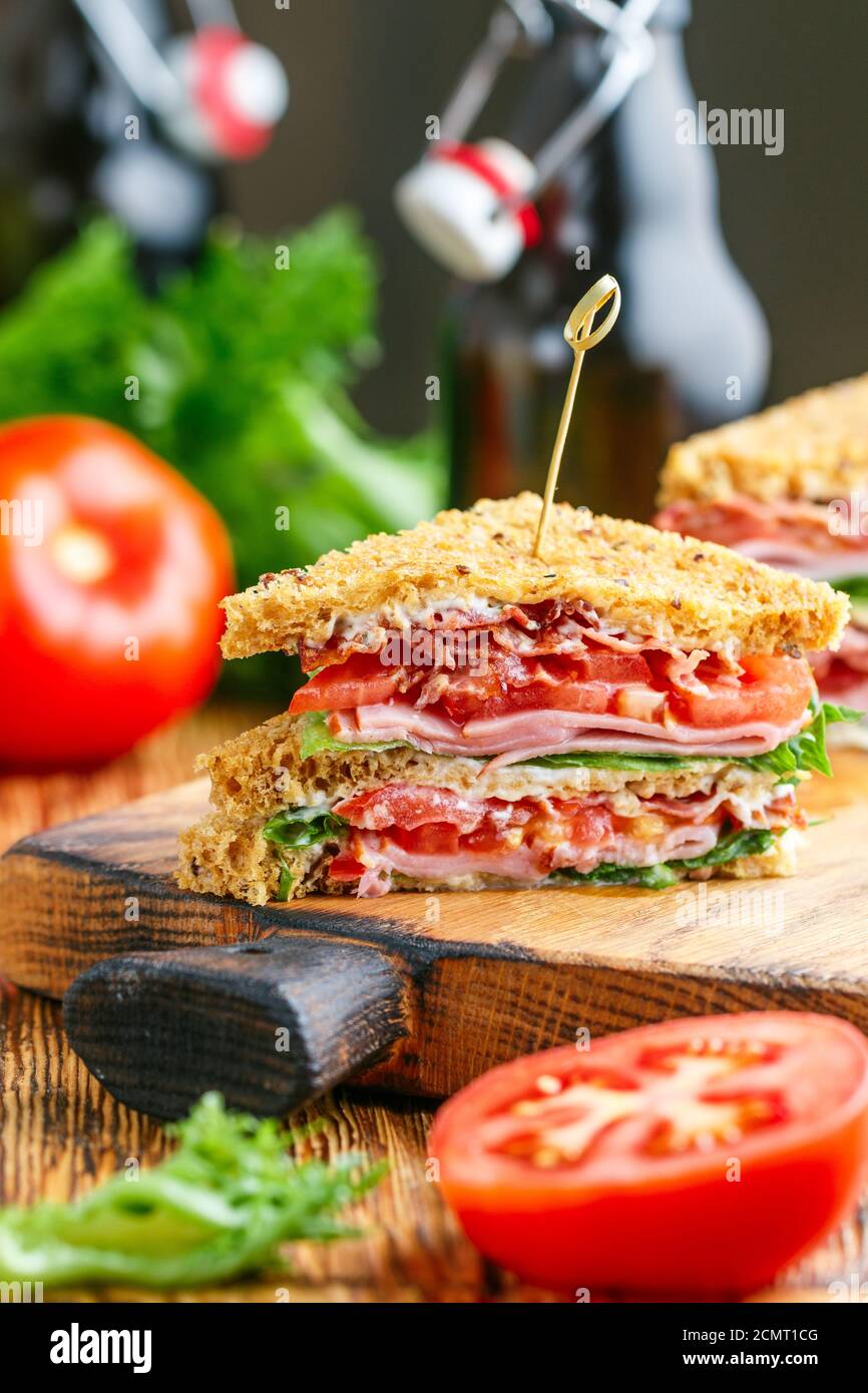 Délicieux sandwichs club avec salade verte laitue, jambon, bacon, tomates fraîches et sauce sur une planche à découper en bois. Concept déjeuner. Mise au point sélective Banque D'Images