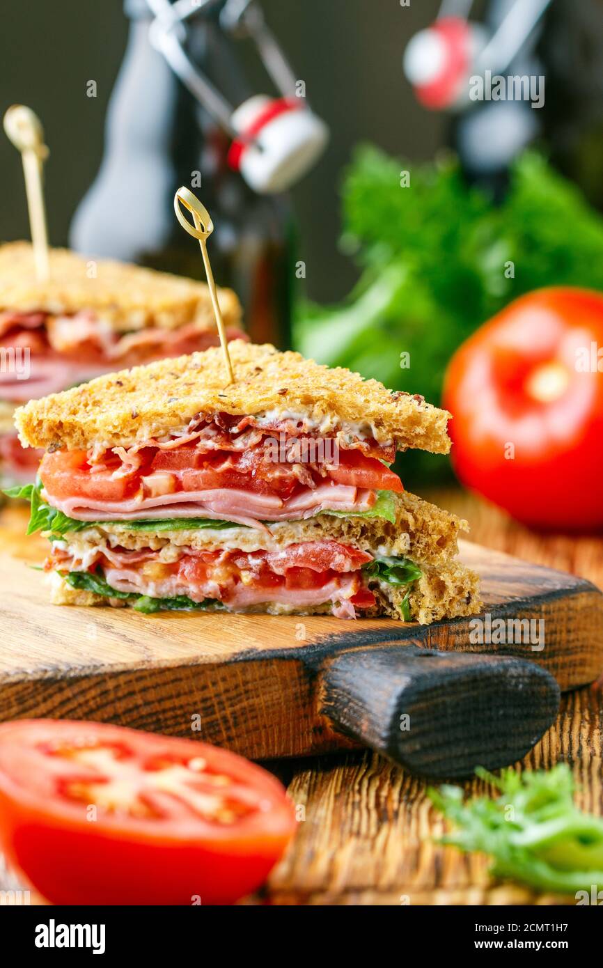 Délicieux sandwichs club avec salade verte laitue, jambon, bacon, tomates fraîches et sauce sur une planche à découper en bois. Concept déjeuner. Mise au point sélective Banque D'Images