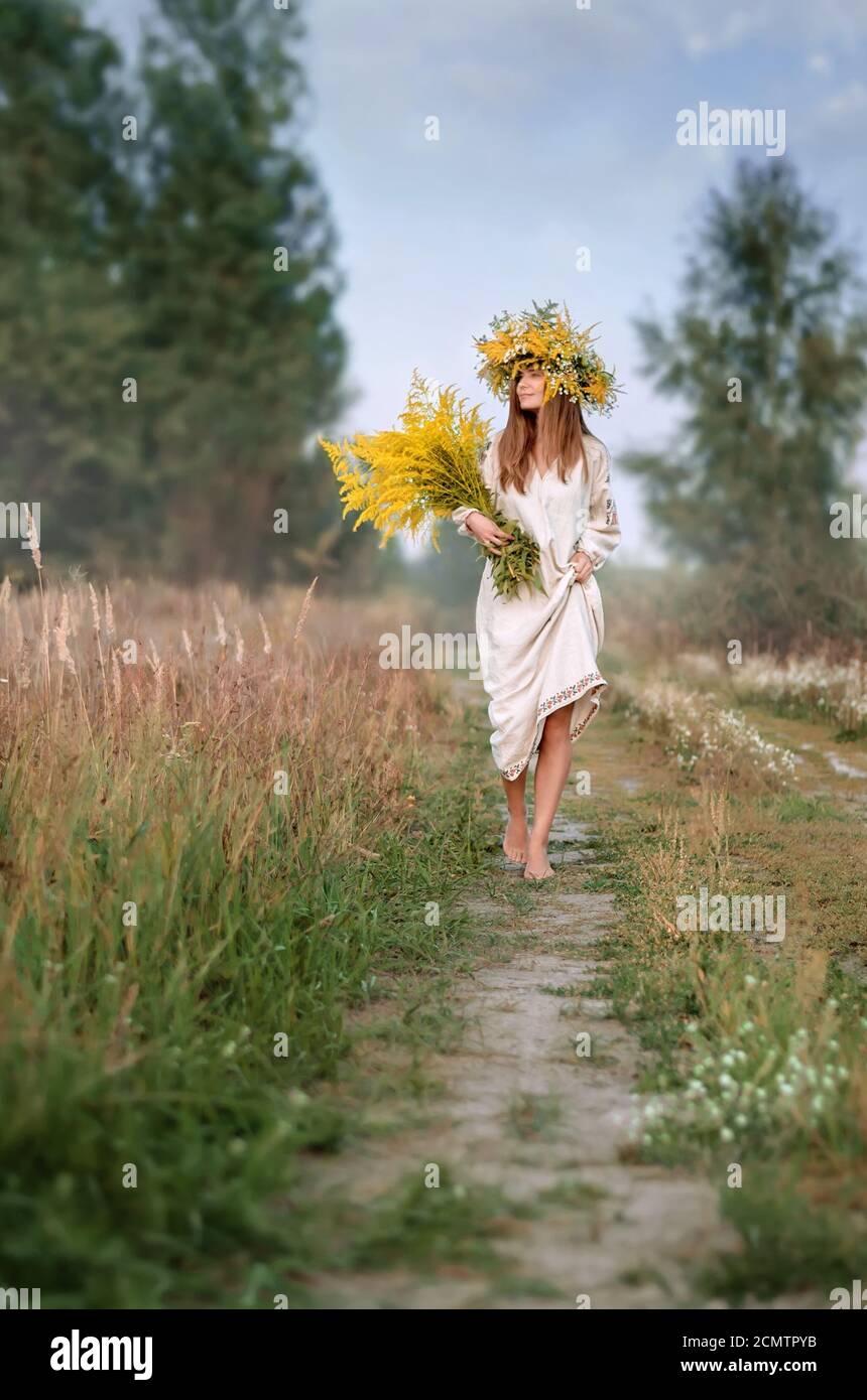 Belle fille dans une couronne de fleurs sauvages et un ancien vêtements brodés avec un grand bouquet marchant pieds nus sur le chemin. Vacances à Ivana Kupala Banque D'Images