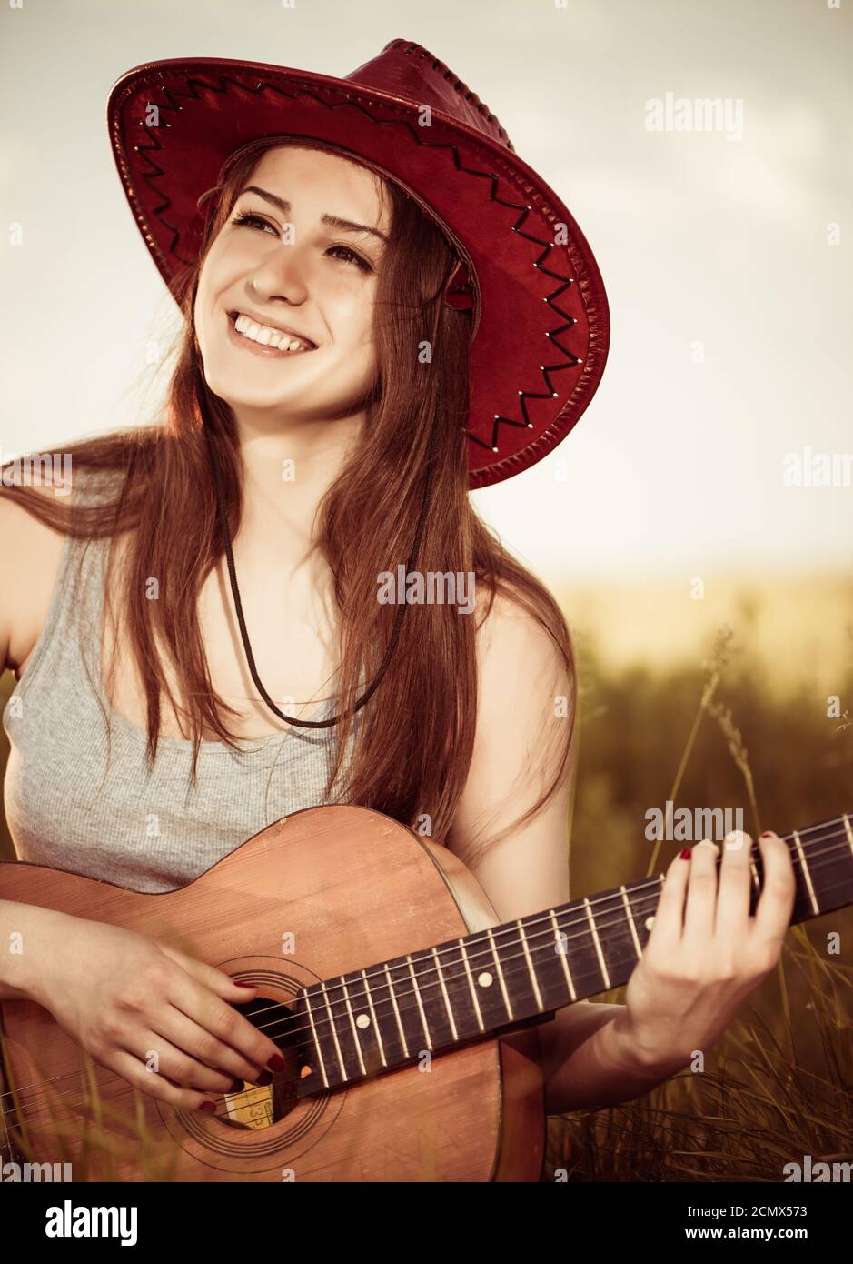 jeune femme en chapeau avec guitare acoustique au pré de printemps Banque D'Images