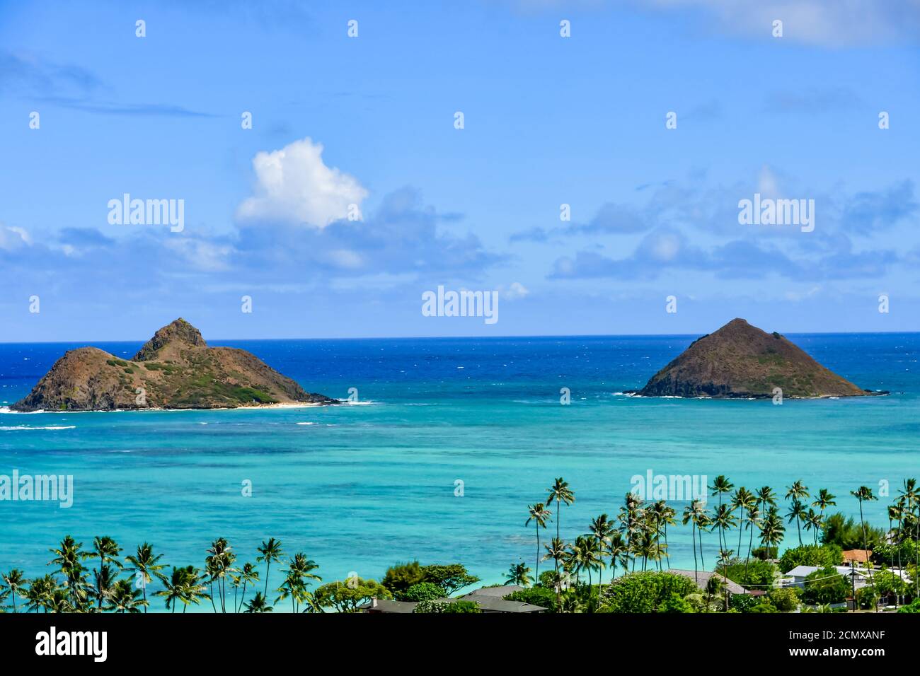 Bleu clair de l'eau de l'océan et deux petites îles. Palmiers sur la plage et maisons. Ciel bleu avec nuages blancs à Hawaï. Banque D'Images