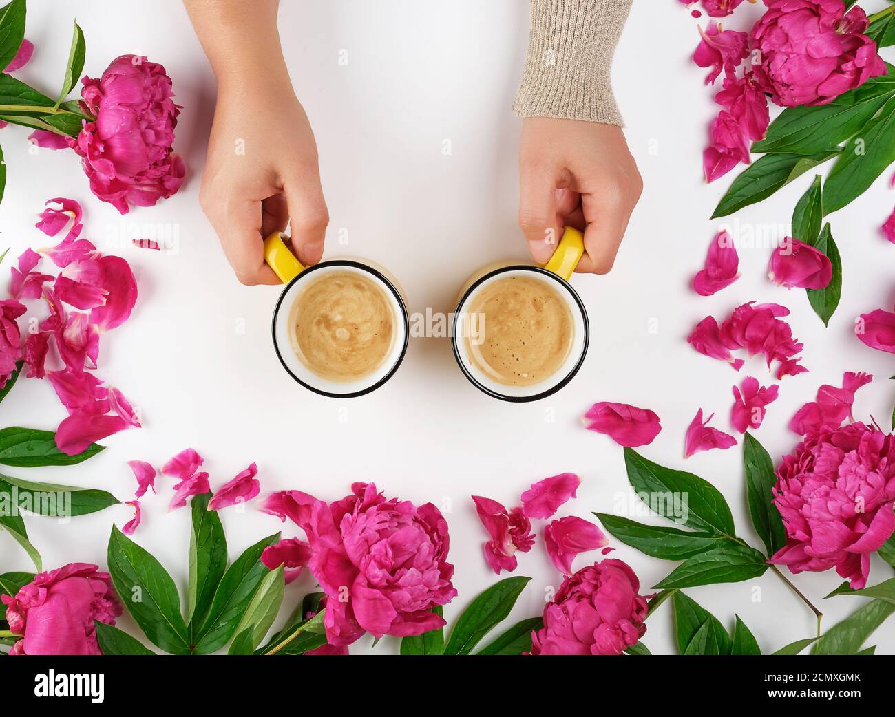 deux mains tenant des tasses jaunes avec une boisson chaude au café sur un fond blanc au milieu de la floraison Banque D'Images