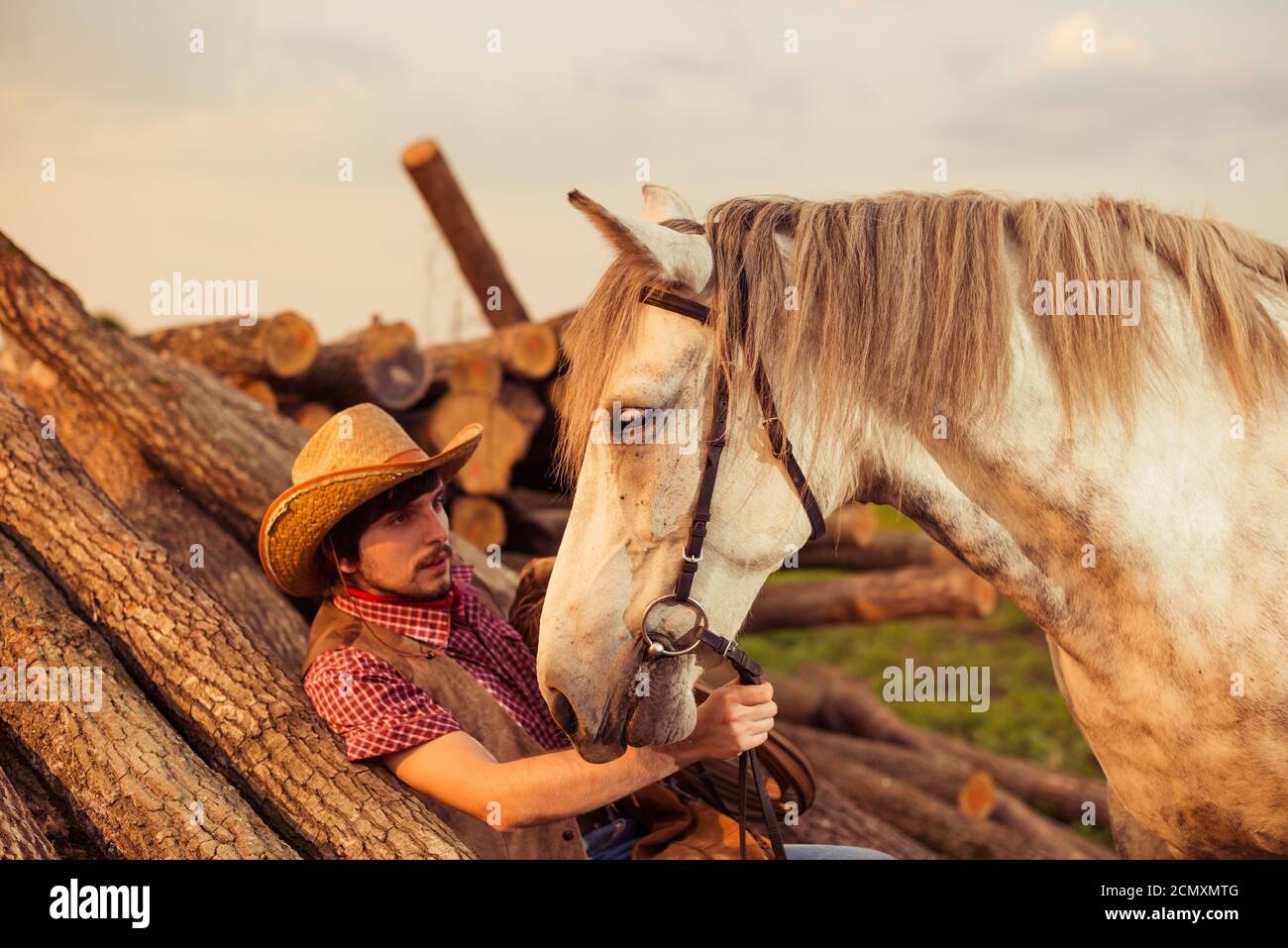 Jeune homme en chapeau et cheval blanc à la ferme d'été coucher de soleil Banque D'Images