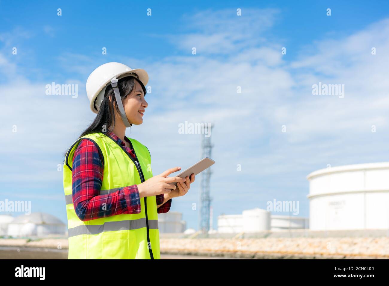 Femme asiatique ingénieur pétrochimique travaillant avec une tablette numérique dans l'usine de raffinage de pétrole et de gaz la nuit pour la sécurité des inspecteurs Banque D'Images