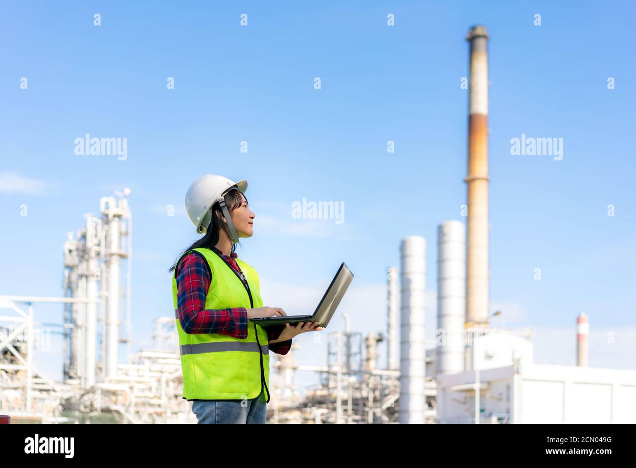 Femme asiatique ingénieur pétrochimique travaillant la nuit avec un ordinateur portable dans l'usine de raffinage de pétrole et de gaz la nuit pour la sécurité des inspecteurs Banque D'Images