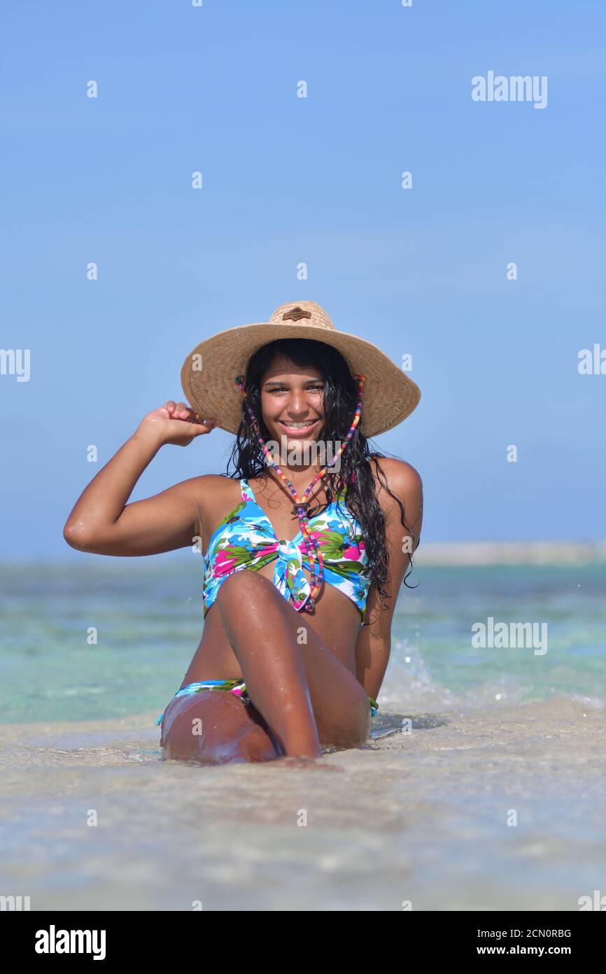 Femme hispanique se trouvant sur la plage à l'intérieur d'une éclaboussure d'eau bleue. Rire naturel tenant chapeau de paille , Beach arrière-plan Los Roques Venezuela Banque D'Images