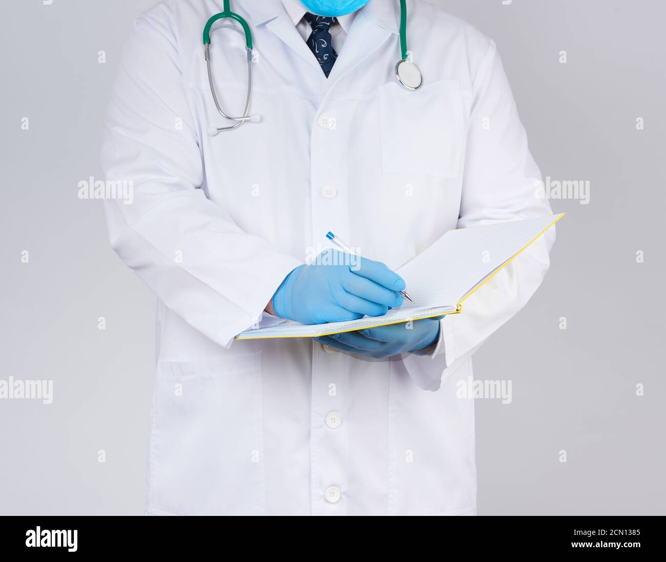 docteur en robe blanche, gants stériles en latex bleu tient un carnet jaune ouvert dans sa main sur un coup Banque D'Images