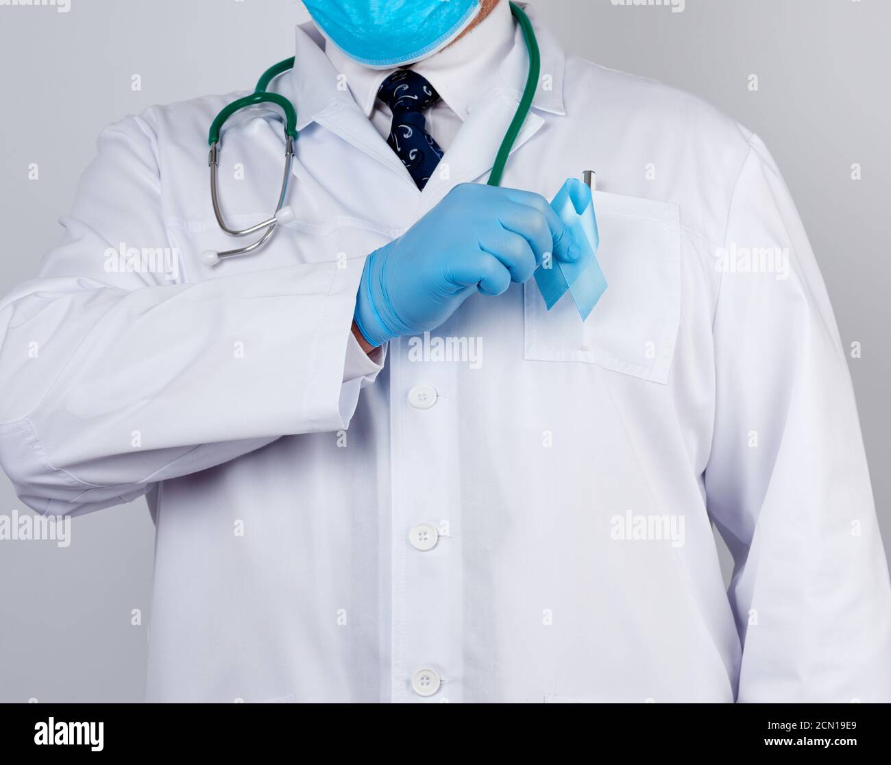 un médecin de sexe masculin est vêtu d'un manteau blanc et d'une cravate.  il tient un ruban en soie bleu dans une boucle, portant une veste bleue  Photo Stock - Alamy