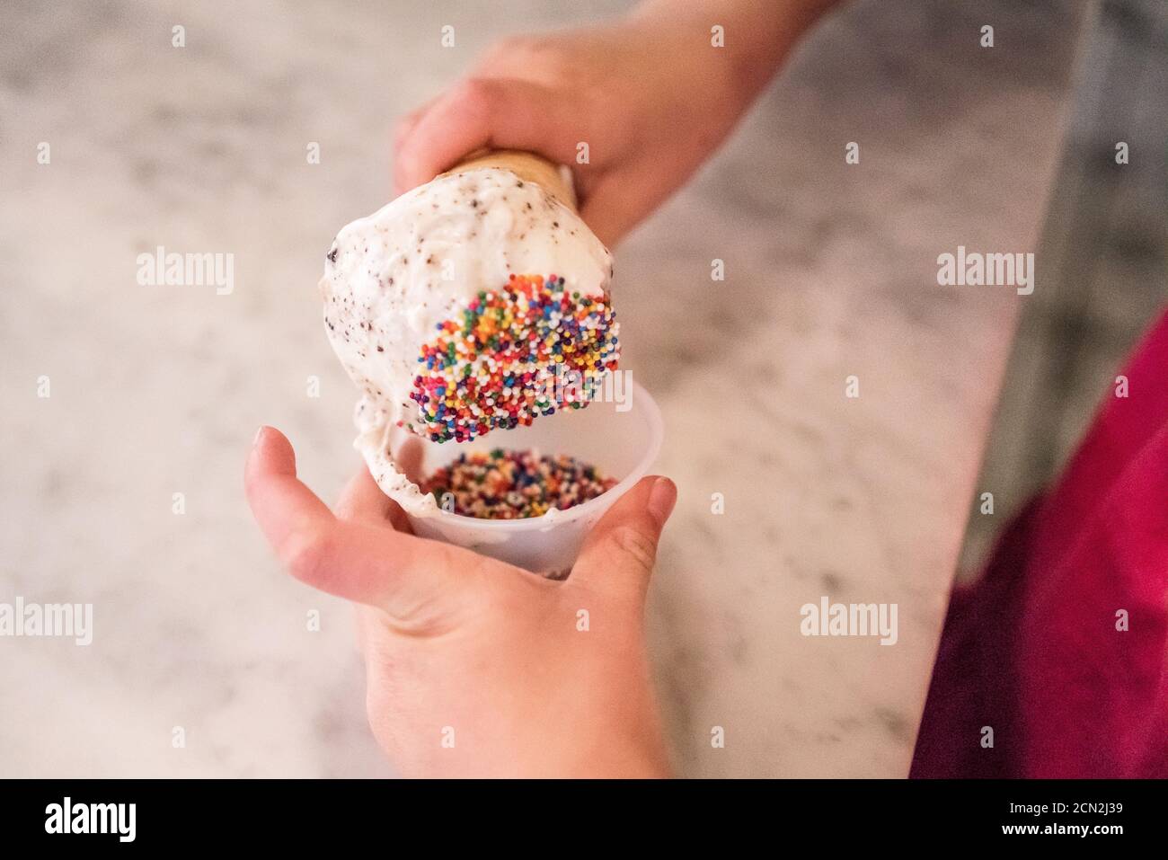 une jeune fille trempent son cône de crème glacée dans un contenant de saupoudrer de couleur Banque D'Images
