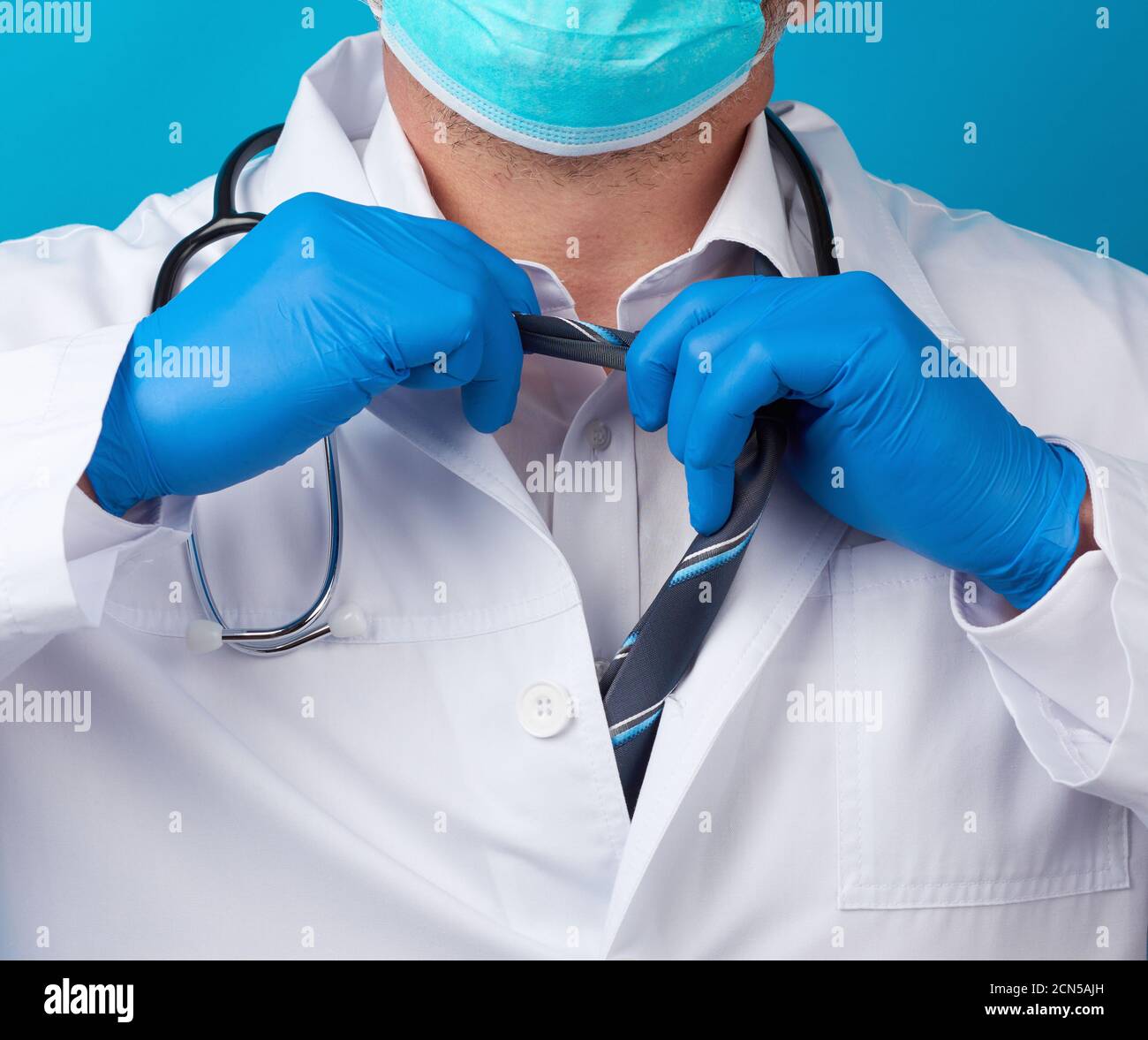 un médecin de sexe masculin dans un manteau blanc se déchire de sa cravate, fond bleu Banque D'Images