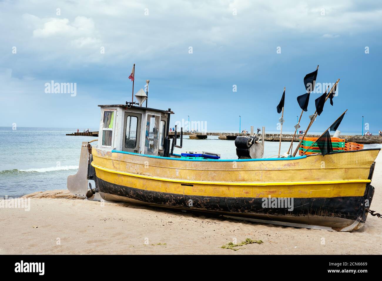 Bateau de pêche rouillé sur une plage de sable avec jetée et bleu mer en arrière-plan Banque D'Images