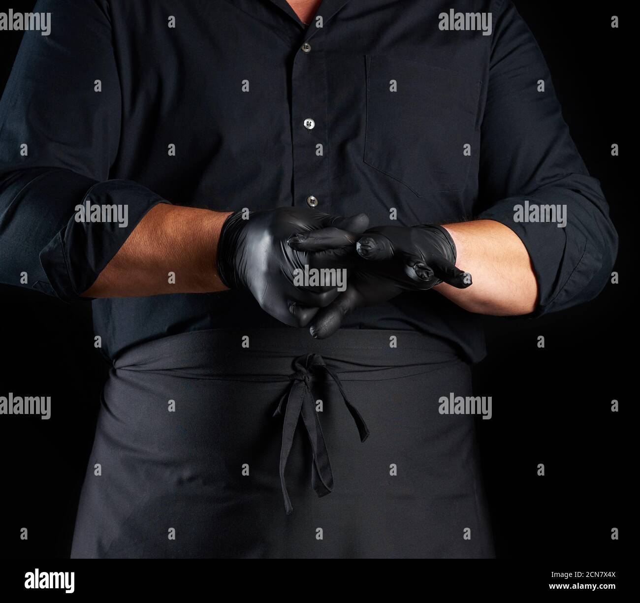 chef en chemise et tablier noirs met des gants en latex noir sur ses mains avant de préparer la nourriture Banque D'Images