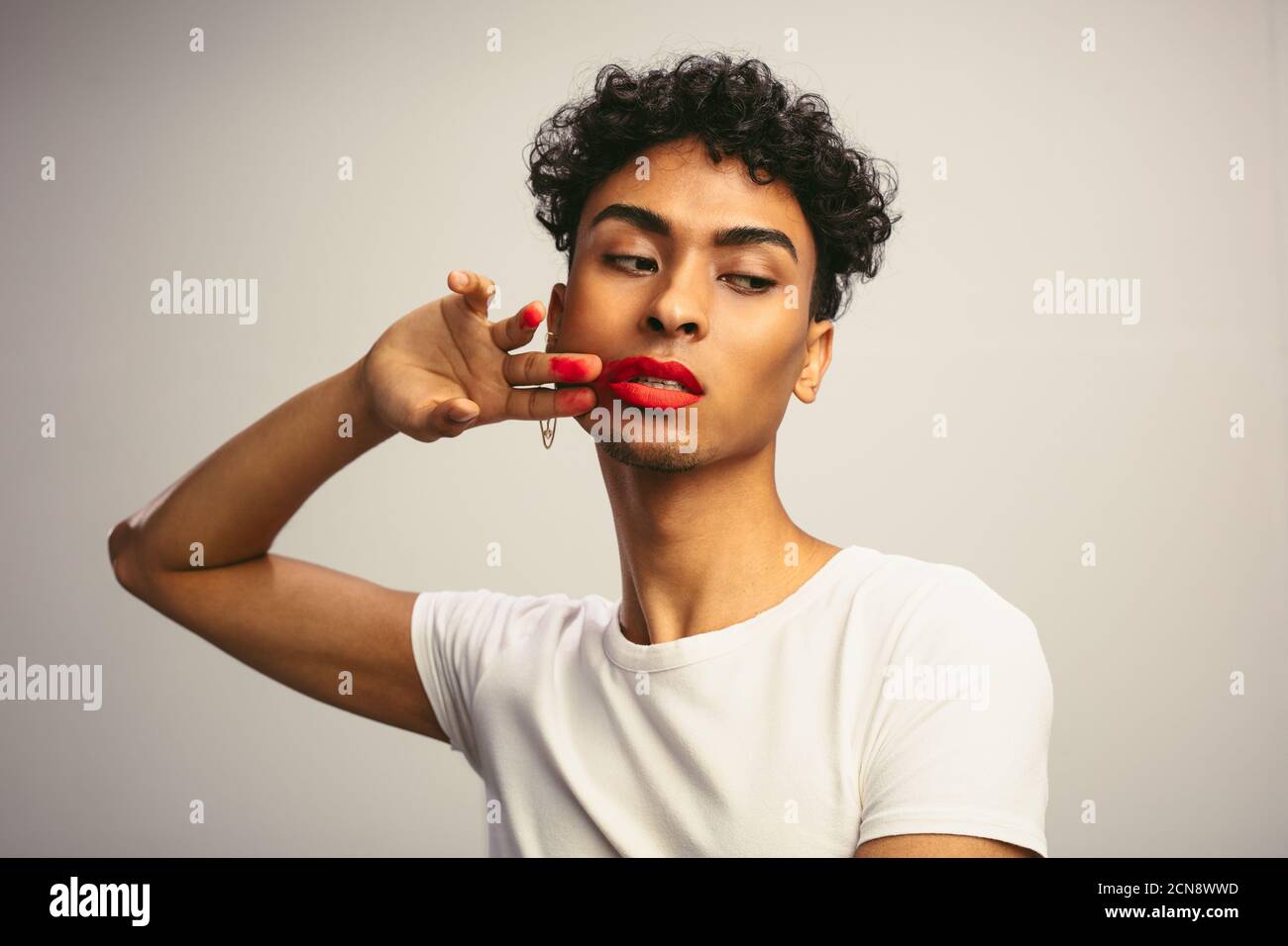 Homme transgenre soupira son rouge à lèvres. Un jeune homme se matravers un rouge à lèvres sur son visage sur fond blanc. Banque D'Images