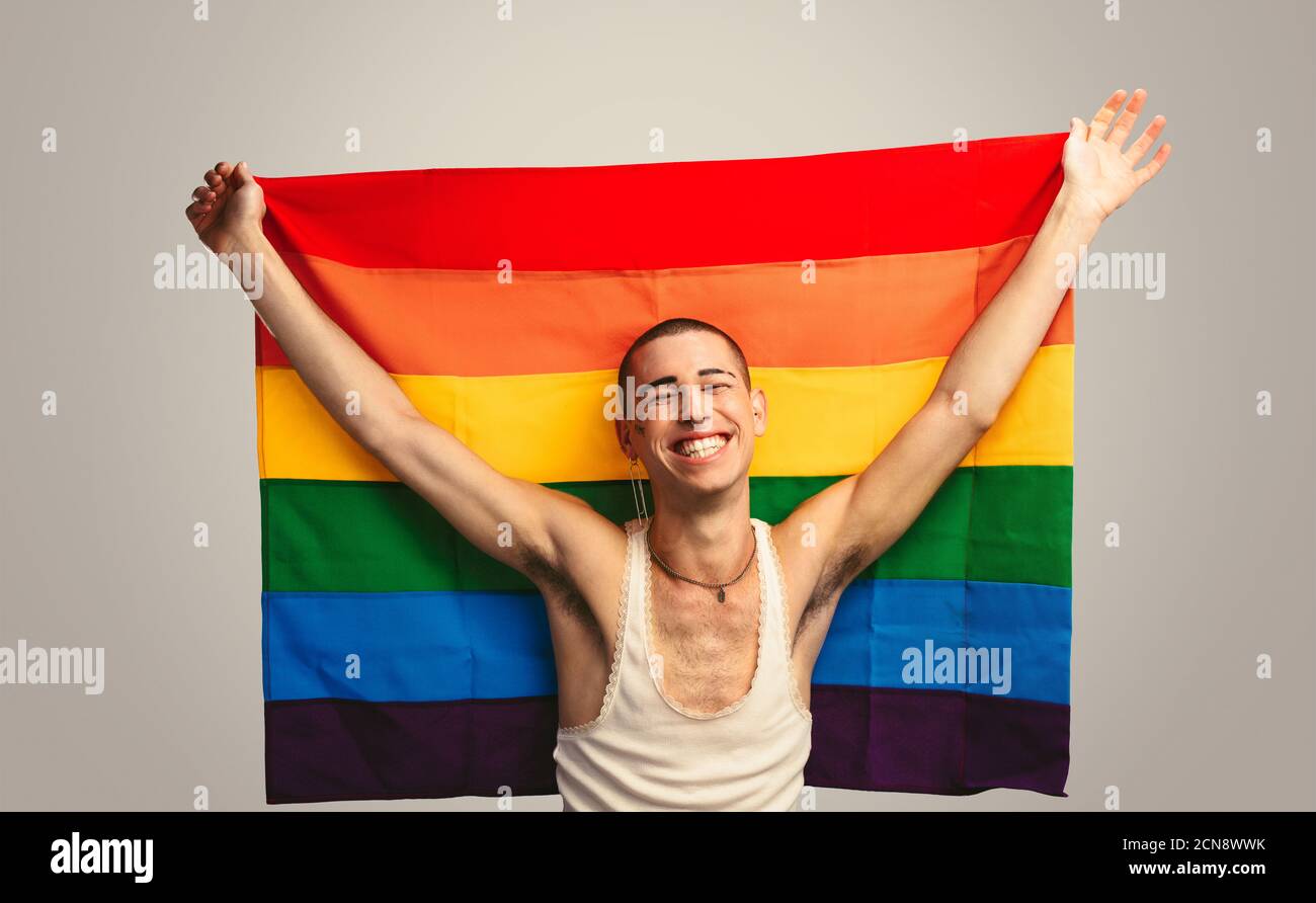 Homme transgenre souriant avec fierté drapeau. Homme joyeux portant un drapeau lgbt sur fond blanc. Banque D'Images