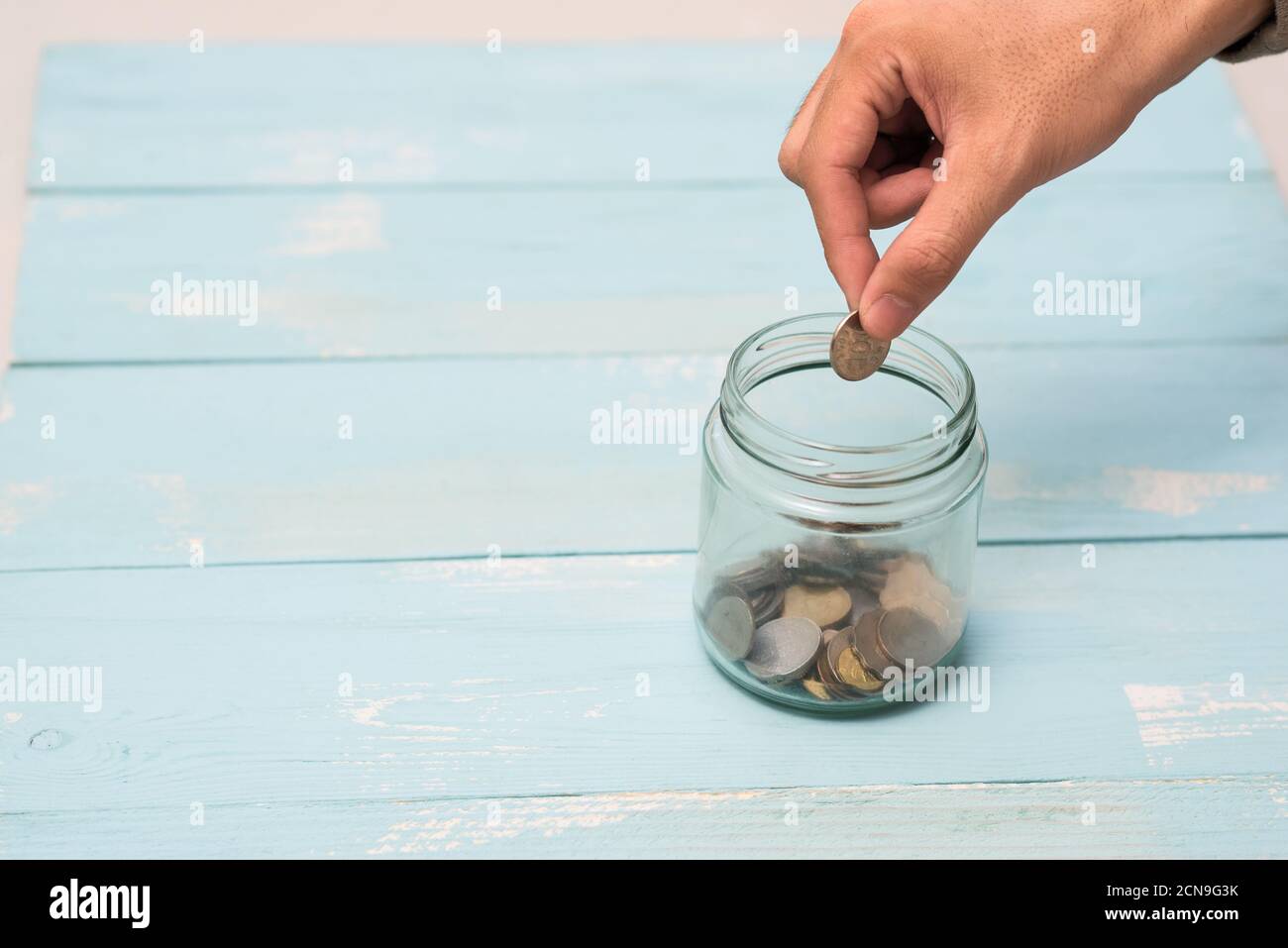 Mettez à la main des pièces de monnaie dans un pot en verre avec une étiquette vide vierge pour le concept de don et de don d'argent Banque D'Images