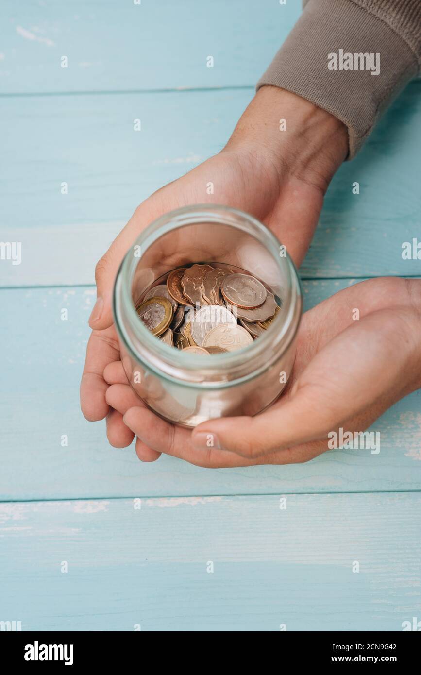 Jeunes mains tenant un pot en verre avec de l'argent (pièces) à l'intérieur Banque D'Images