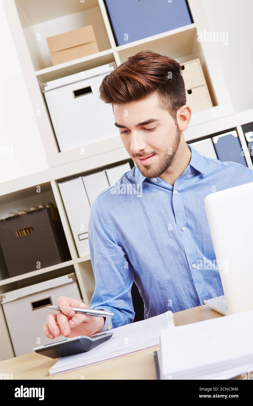 Le jeune homme d'affaires au bureau calcule le financement à l'aide de la calculatrice Banque D'Images