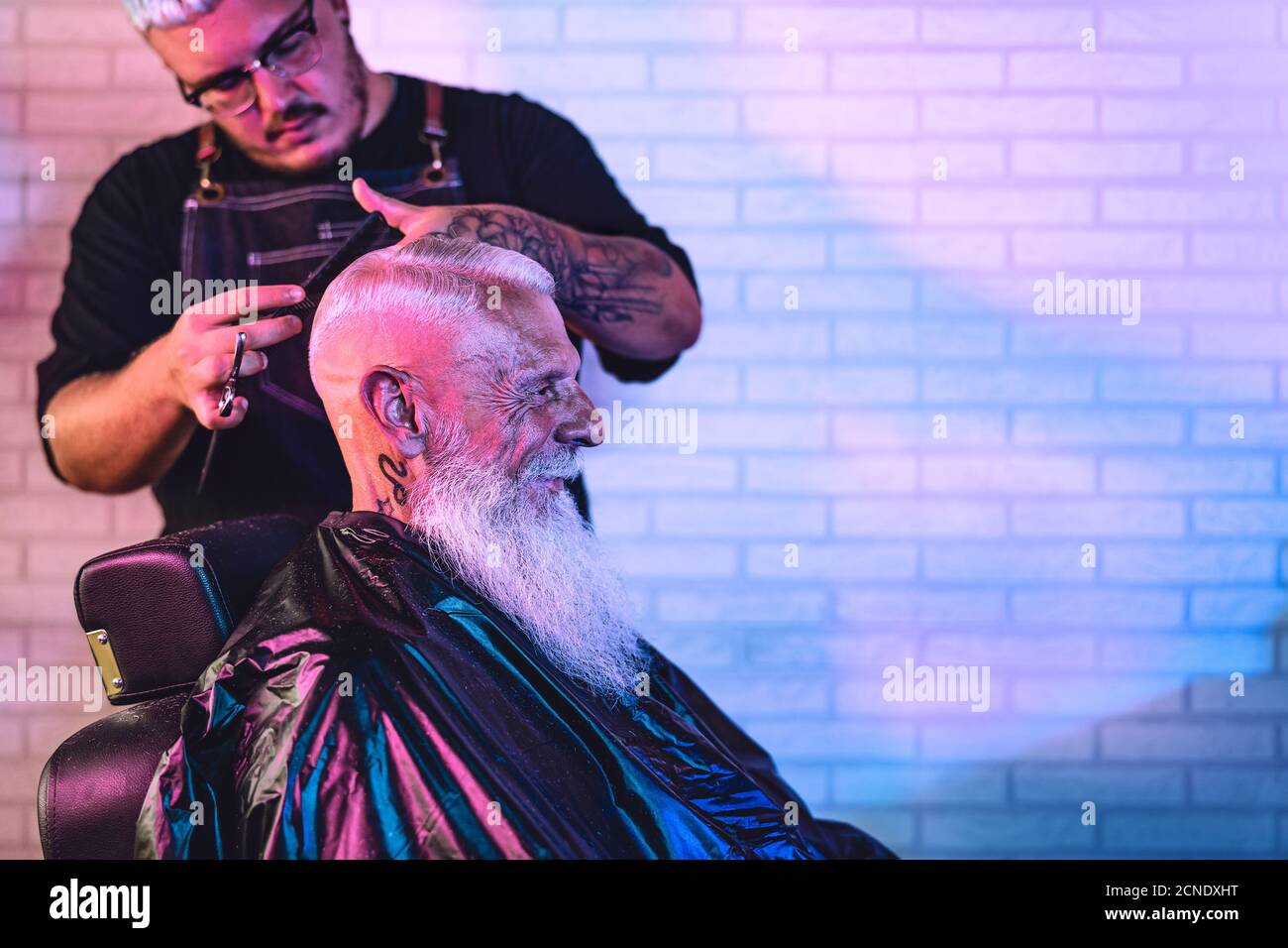 Coiffeur de sexe masculin coupant les cheveux au client principal de l'hipster - côté vue de la jeune coiffeuse travaillant dans un salon de coiffure Banque D'Images