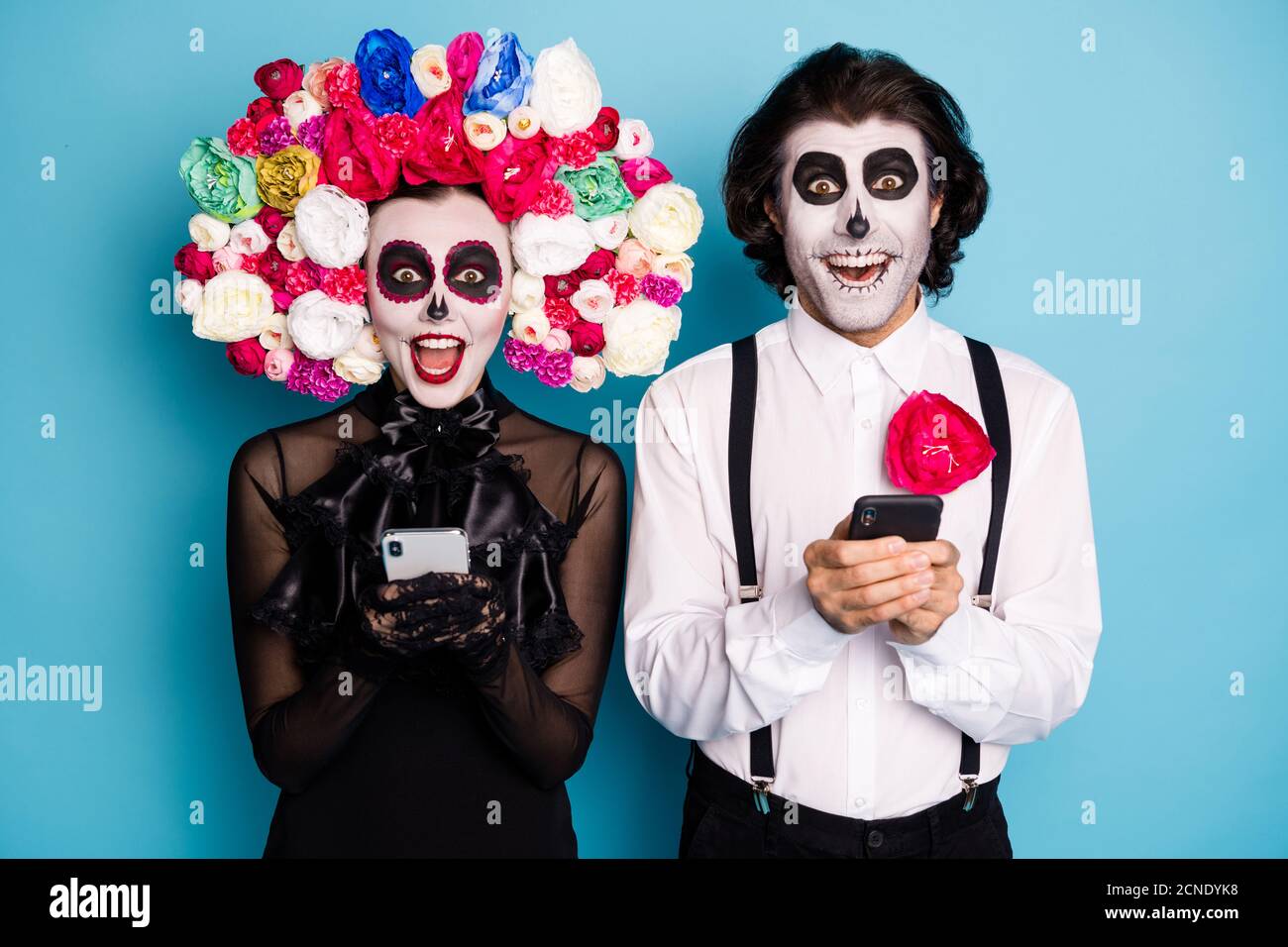 Photo de démon effrayant couple homme femme tenir les téléphones excités trouver la voie devenir des fantômes dent ami porter noir robe mort bandeau de roses de costume Banque D'Images