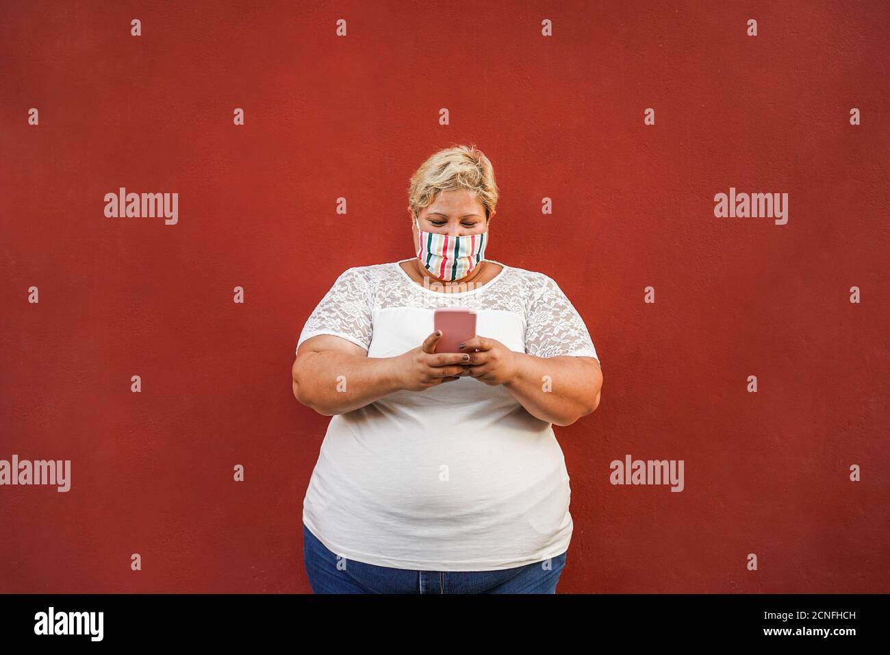 Femme curvy utilisant un smartphone extérieur portant un masque de protection du visage - Concept de mode de vie du coronavirus Banque D'Images