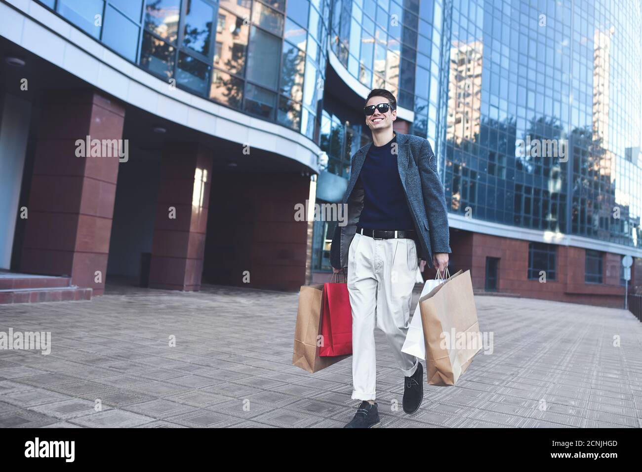 Joyeux jeune homme élégant marchant dans la rue urbaine et appréciant les magasins du Vendredi fou dans les magasins branchés de la ville. Banque D'Images