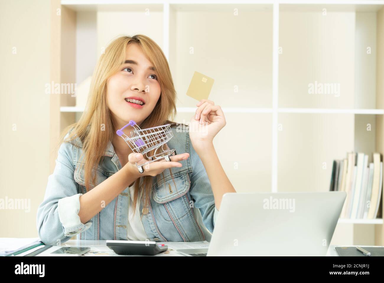 Beautiful woman holding credit card à la maison et penser à des magasins Les magasins en ligne. Concept de modernisation de magasinage en ligne. Banque D'Images
