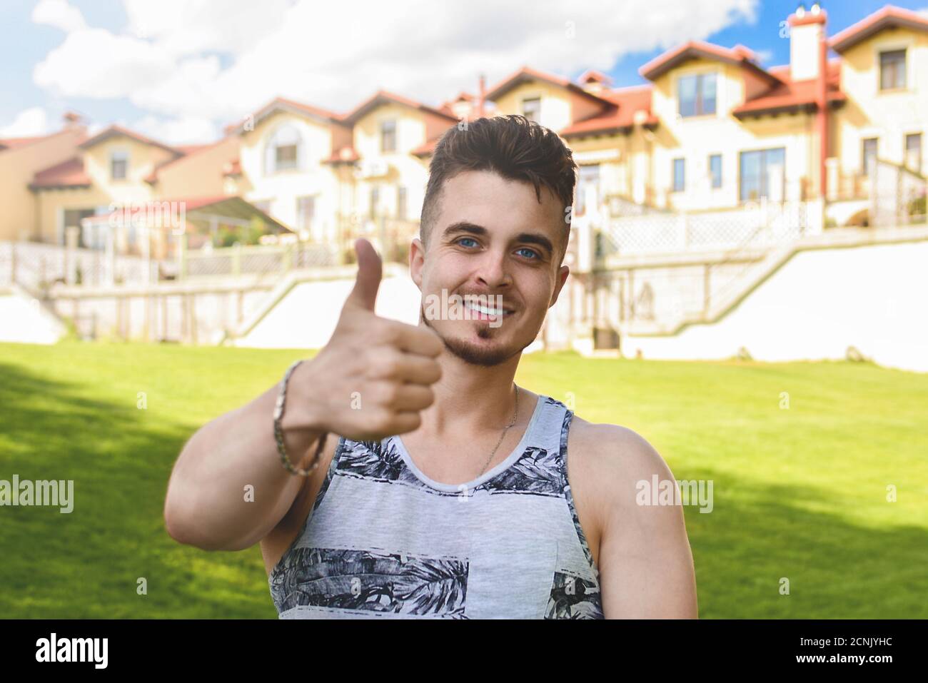 Beau homme de repos avec le pouce vers le haut. Belles cottages en arrière-plan. Banque D'Images