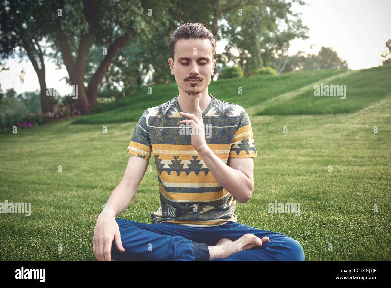 Jeune homme méditant dehors dans le parc, assis avec les yeux fermés et ses mains ensemble.appréciant la nature, le yoga et la méditation Banque D'Images