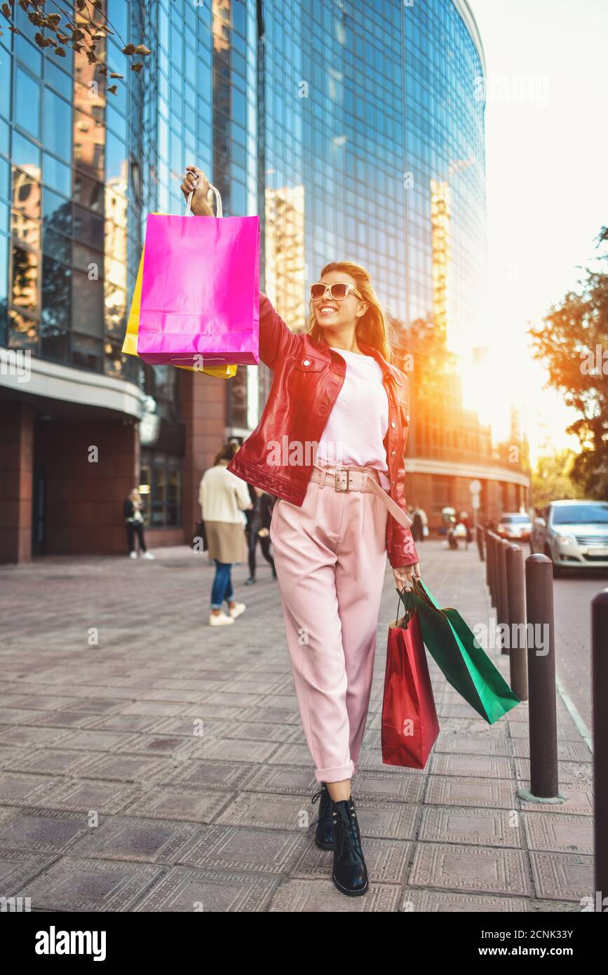 Belle fille souriante dans des lunettes de soleil tient des sacs d'achats et apprécie ses achats. Banque D'Images