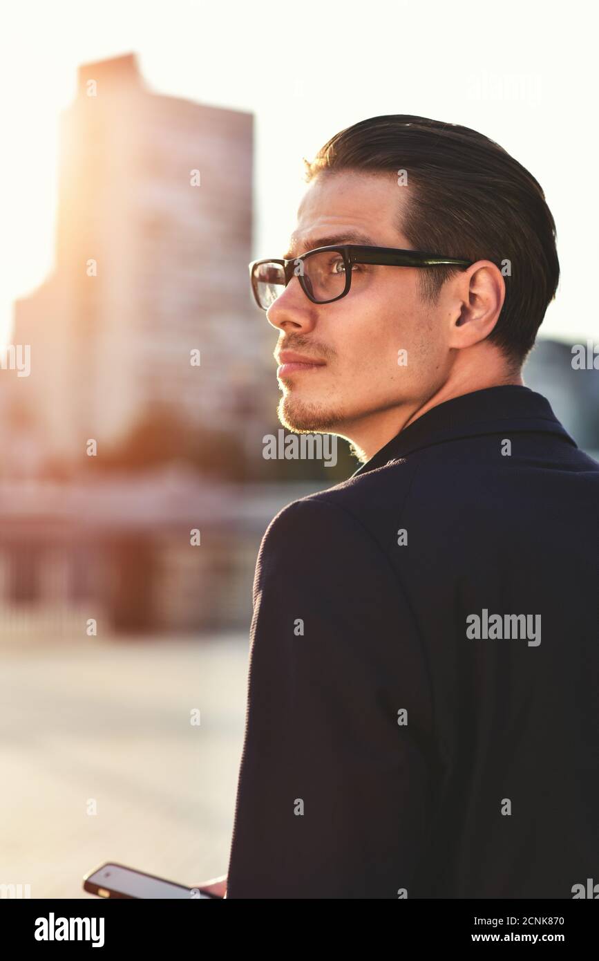 Homme d'affaires prospère dans des supports de lunettes avec téléphone dans une ville moderne. Banque D'Images