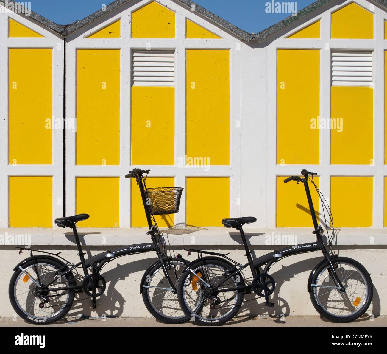 deux vélos noirs reposant sur un mur bas et jaune cabines de plage en arrière-plan Banque D'Images