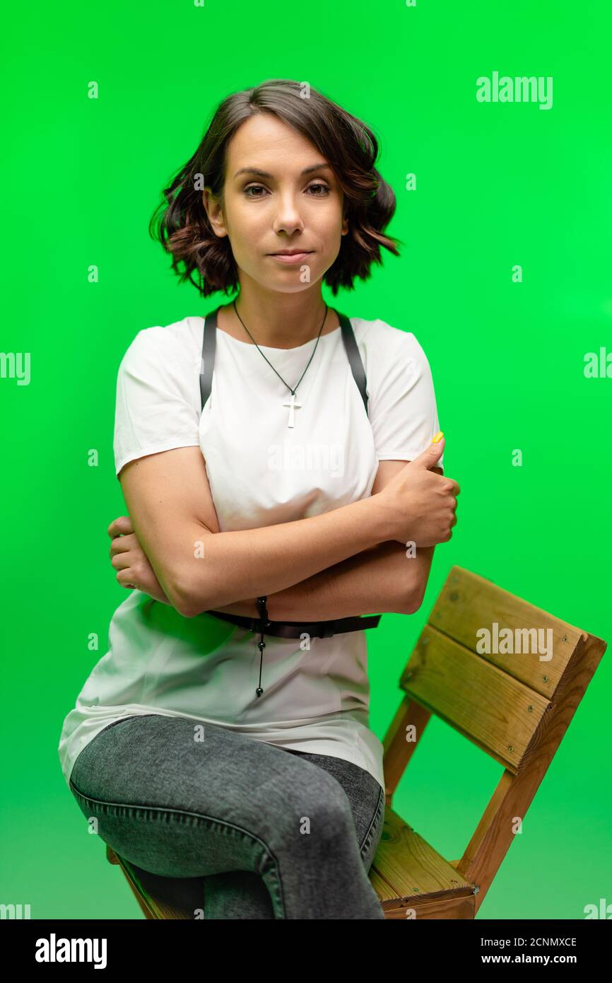 Portrait de femme sur la clé chroma en studio. Femme brune sérieuse en t-shirt blanc posant sur fond vert Banque D'Images