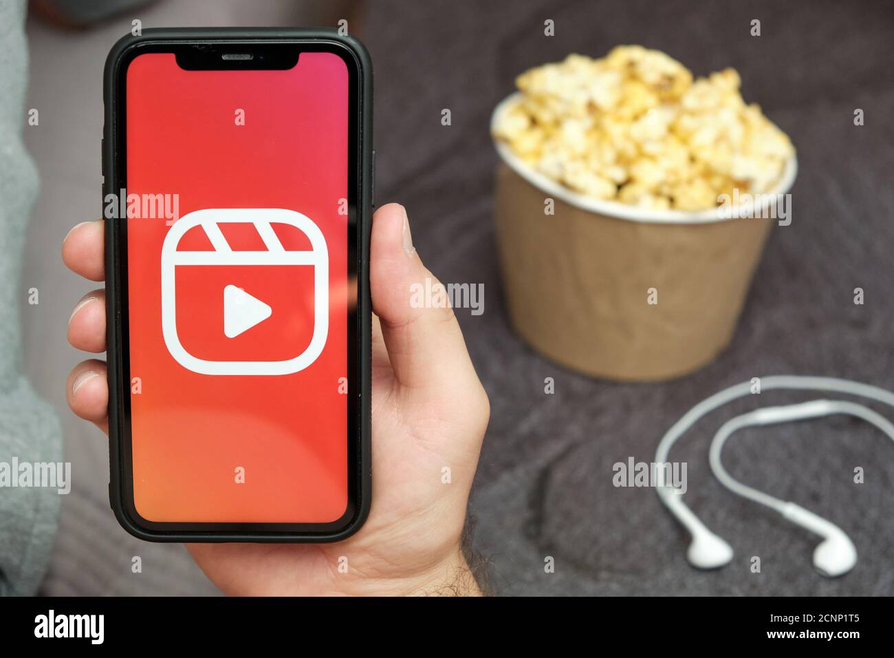 Gros plan les mans tiennent un téléphone portable avec le logo Instagram Reels avec des écouteurs Apple et une boîte pop-corn à côté de lui, août 2020, San Francisco, États-Unis Banque D'Images