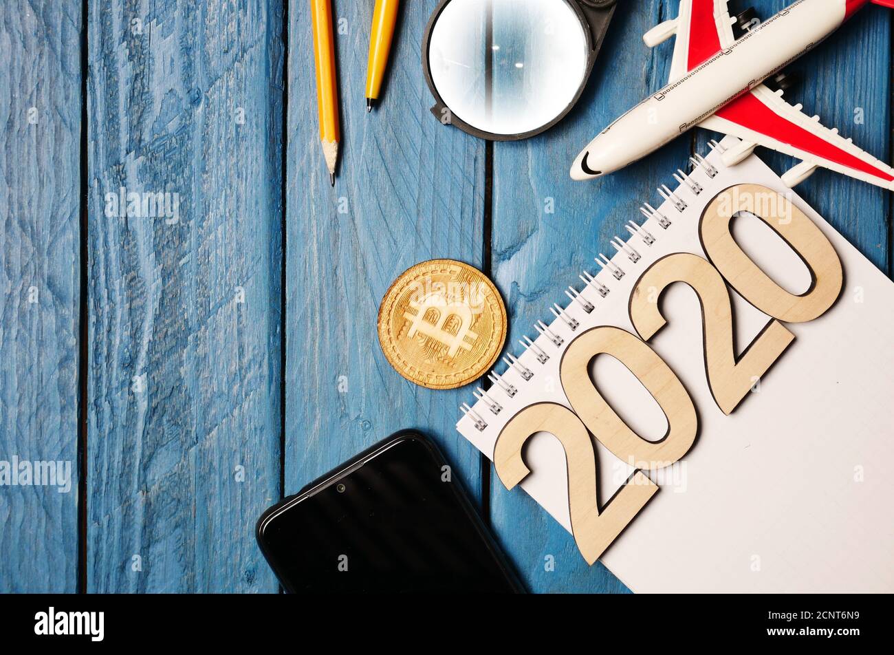 2020 Bloc-notes et stylo en bois avec, bitcoin, smartphone et le modèle d'un jouet avion sur une table en bois bleu, place pour le texte. Banque D'Images