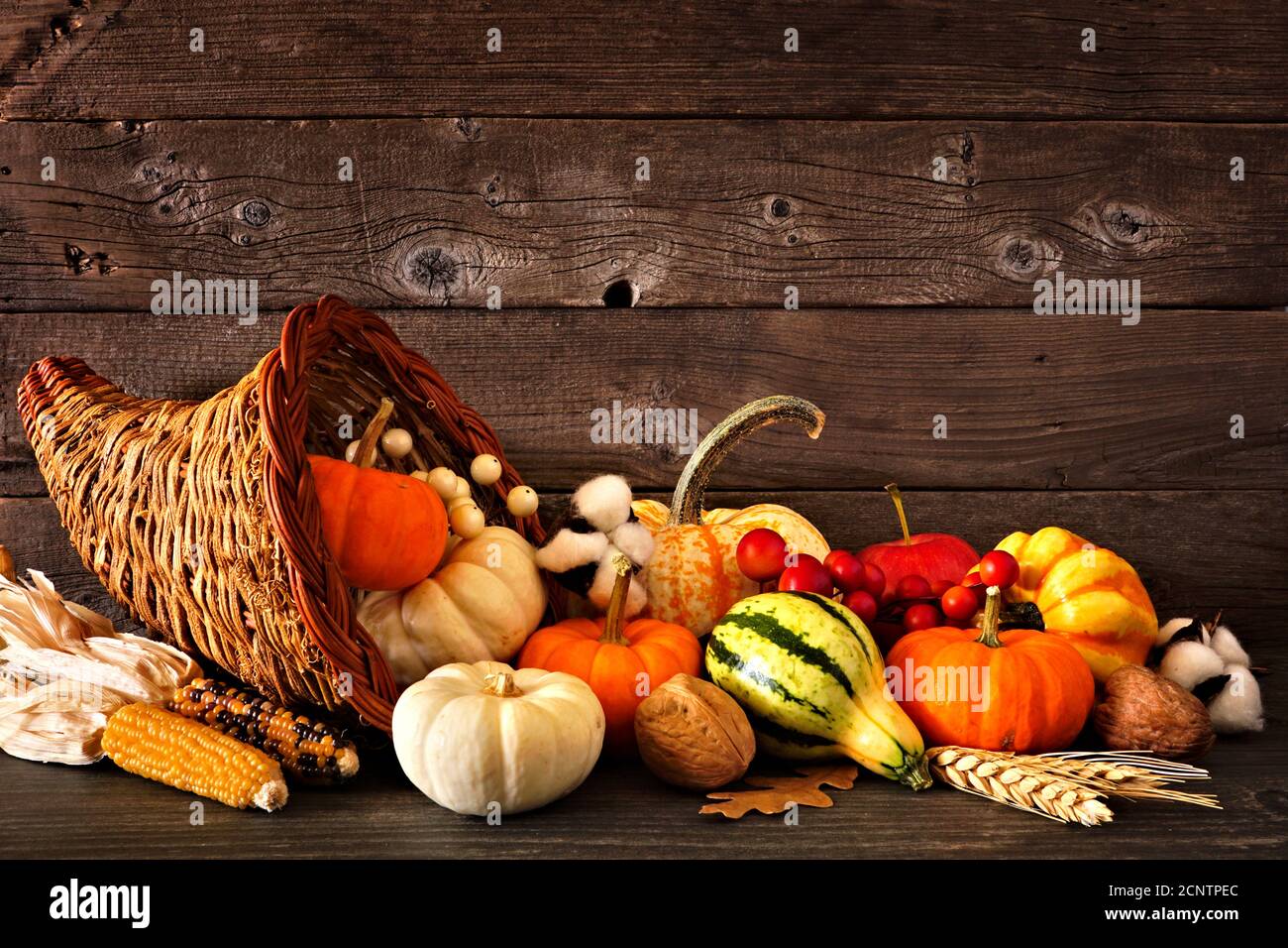 Cornucopia de Thanksgiving remplie de citrouilles d'automne et de légumes contre un arrière-plan rustique en bois sombre Banque D'Images