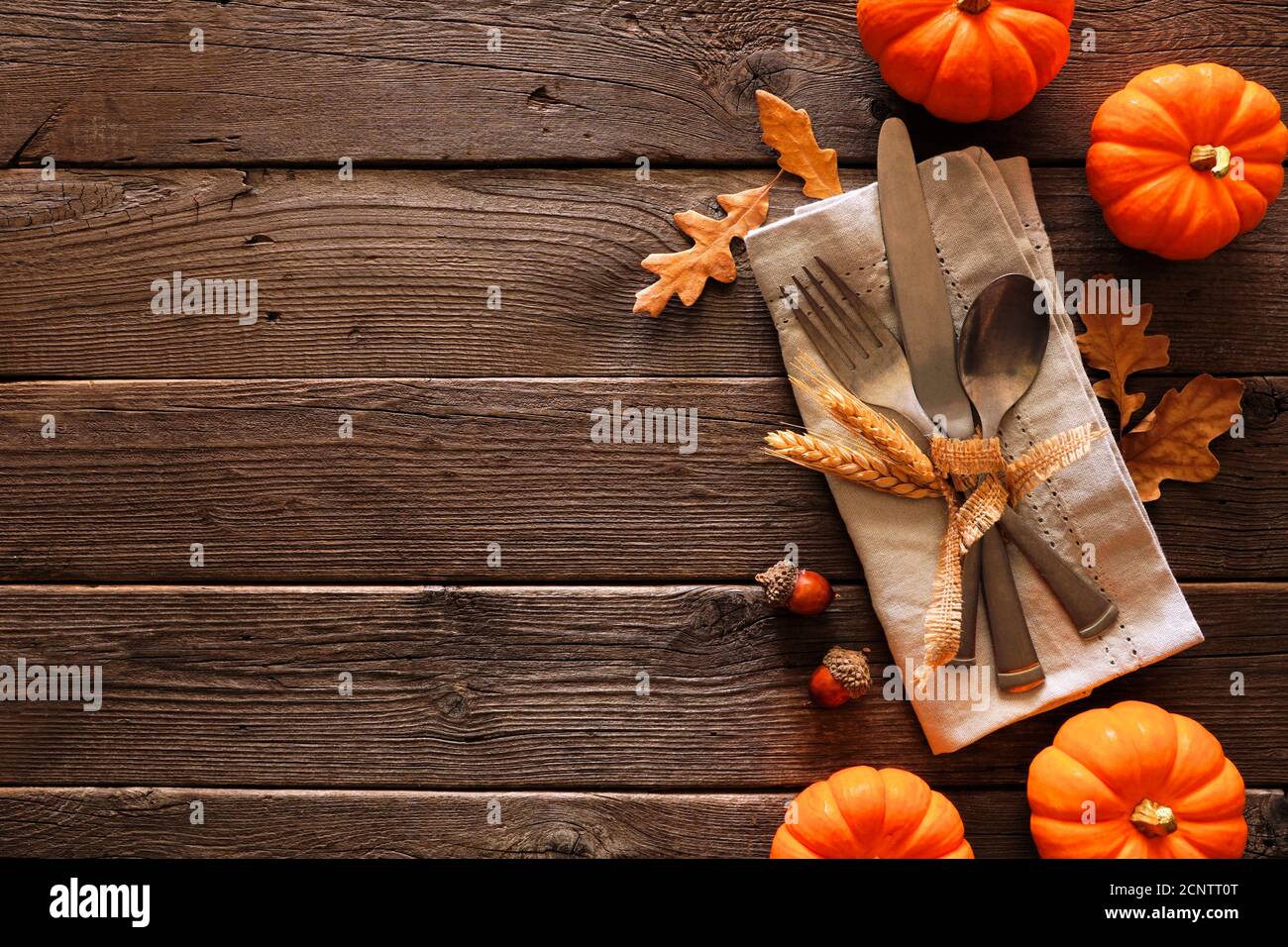 Scène de table de moisson d'automne ou de Thanksgiving avec couverts, serviette, feuilles et citrouille bordent sur un fond rustique en bois sombre Banque D'Images
